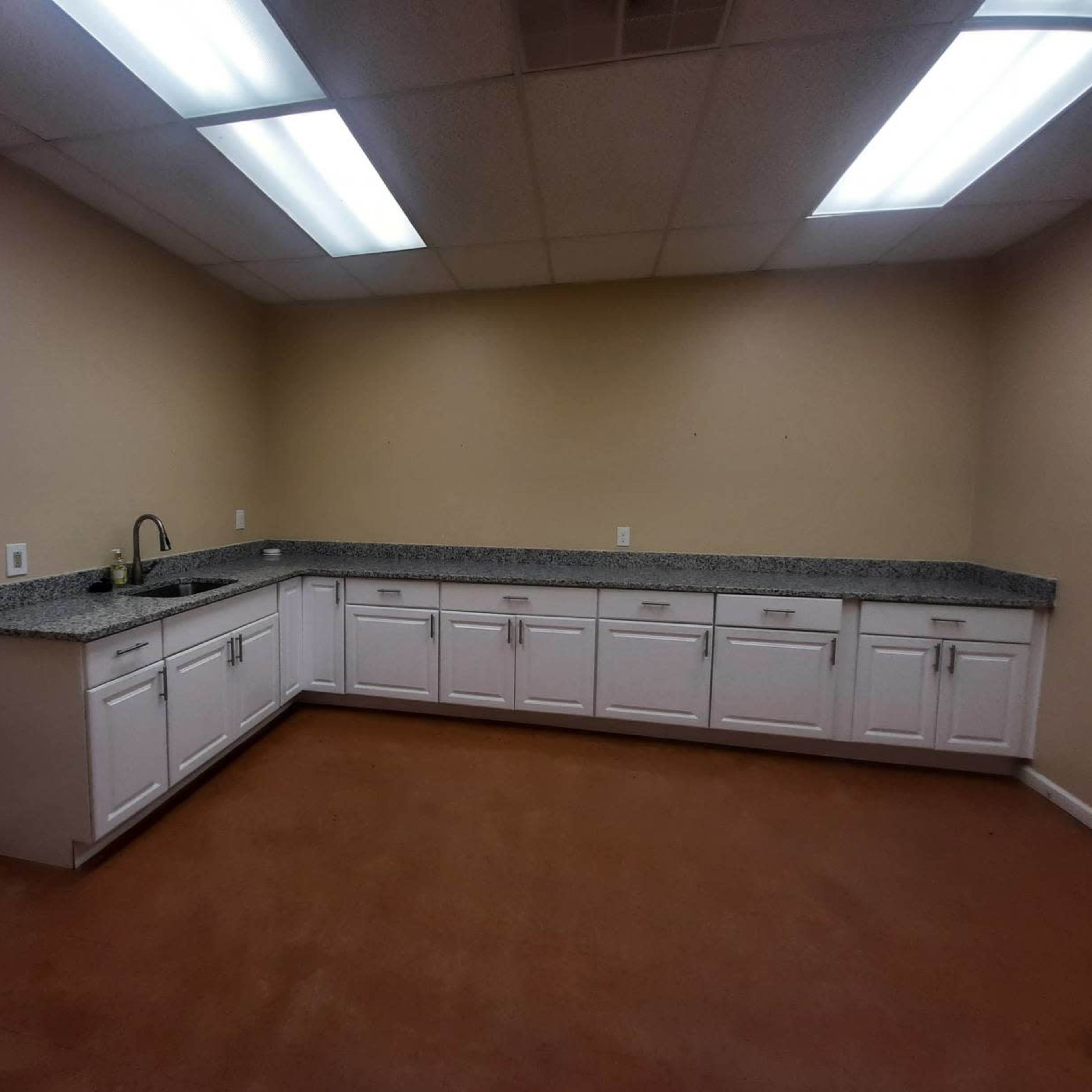 A spacious kitchen with white cabinetry, a long granite countertop, and two fluorescent ceiling lights.