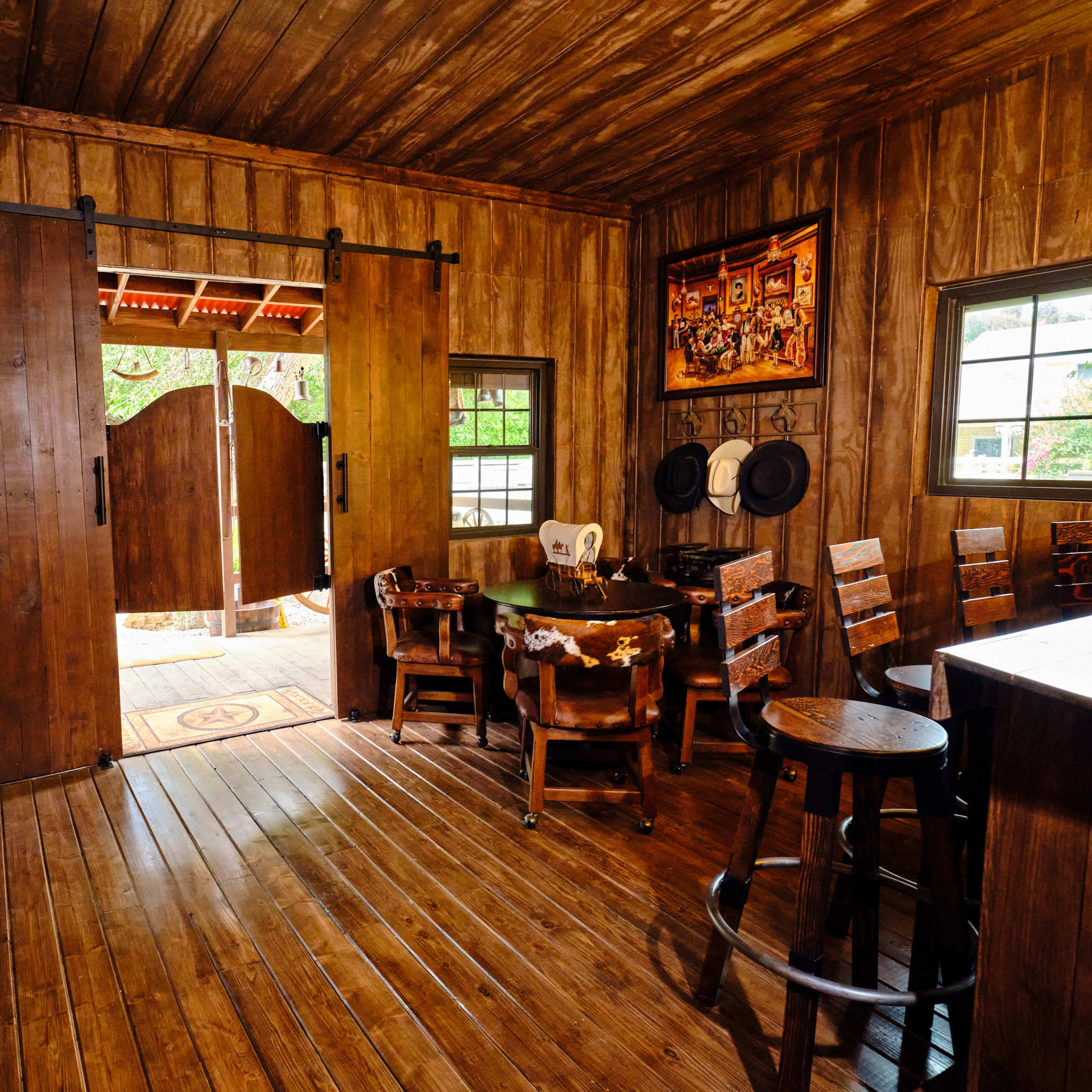 A rustic wooden interior of a room with large sliding barn doors open to an outdoor area, furnished with a dining table and wooden chairs.
