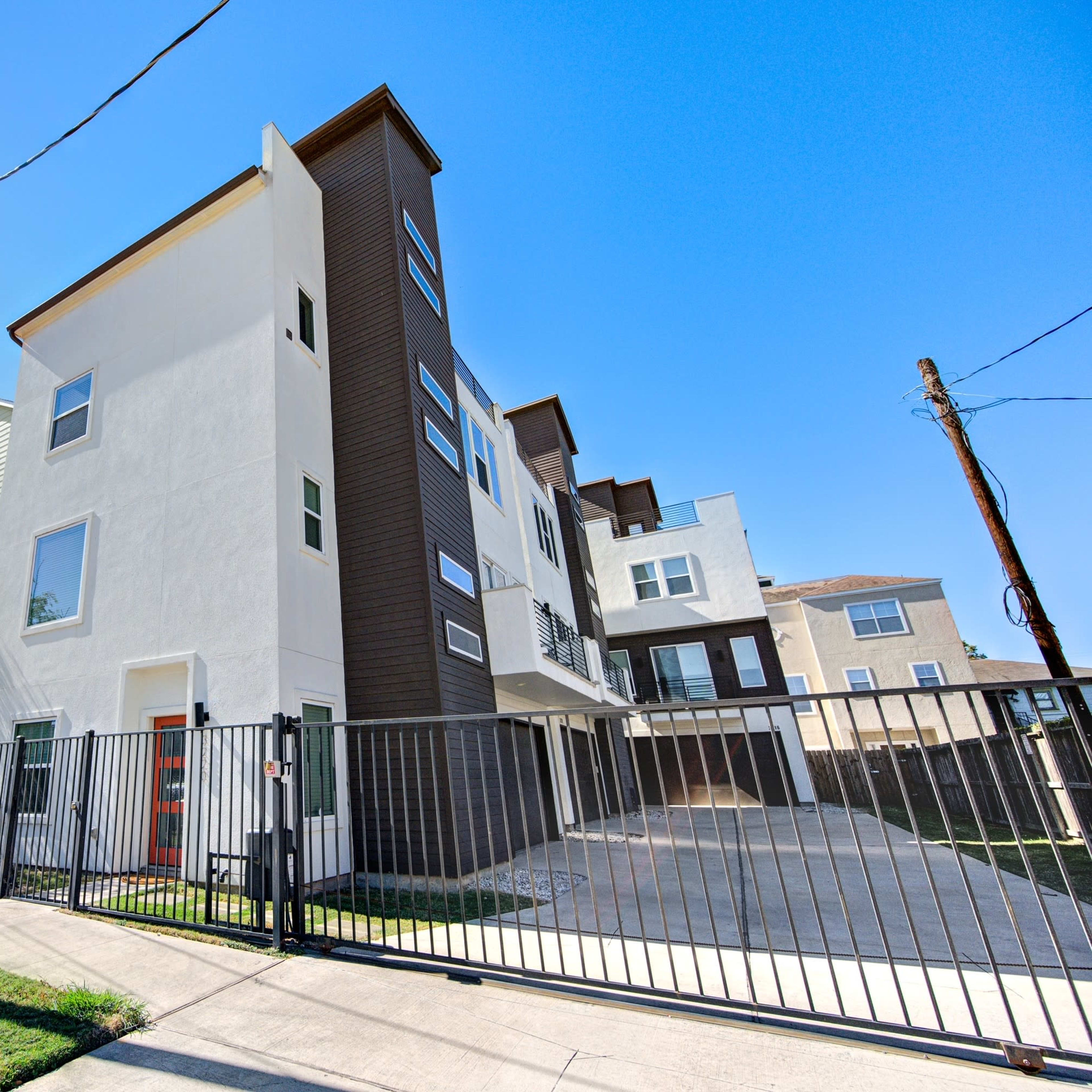 A modern multi-story residential building enclosed by a fence and featuring a gated entrance.