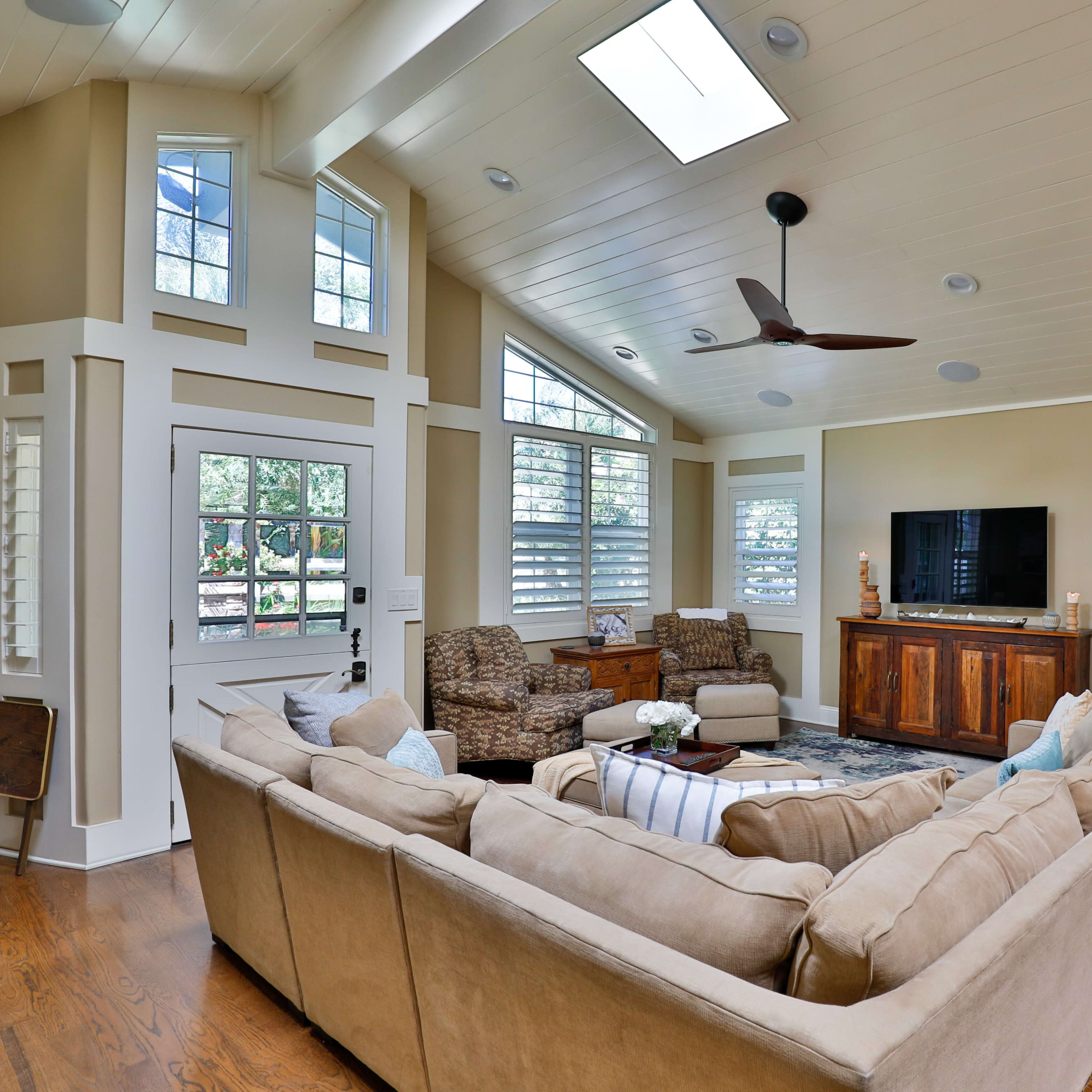 A spacious living room with a large sectional sofa, two armchairs, a wooden entertainment center, and decorative shelves against warm-toned walls.