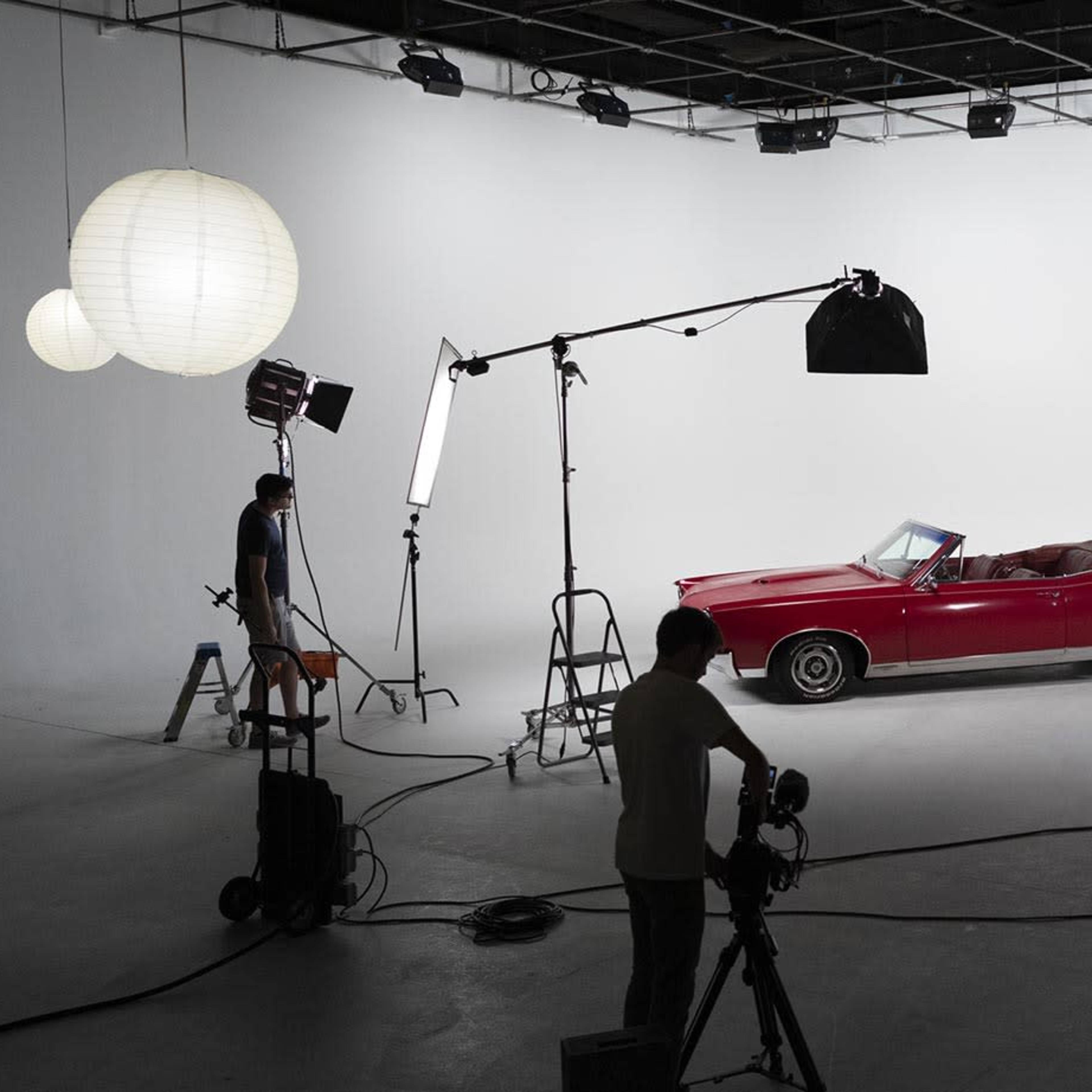 A red convertible car is positioned in a photography studio with various lights and equipment set up around it.