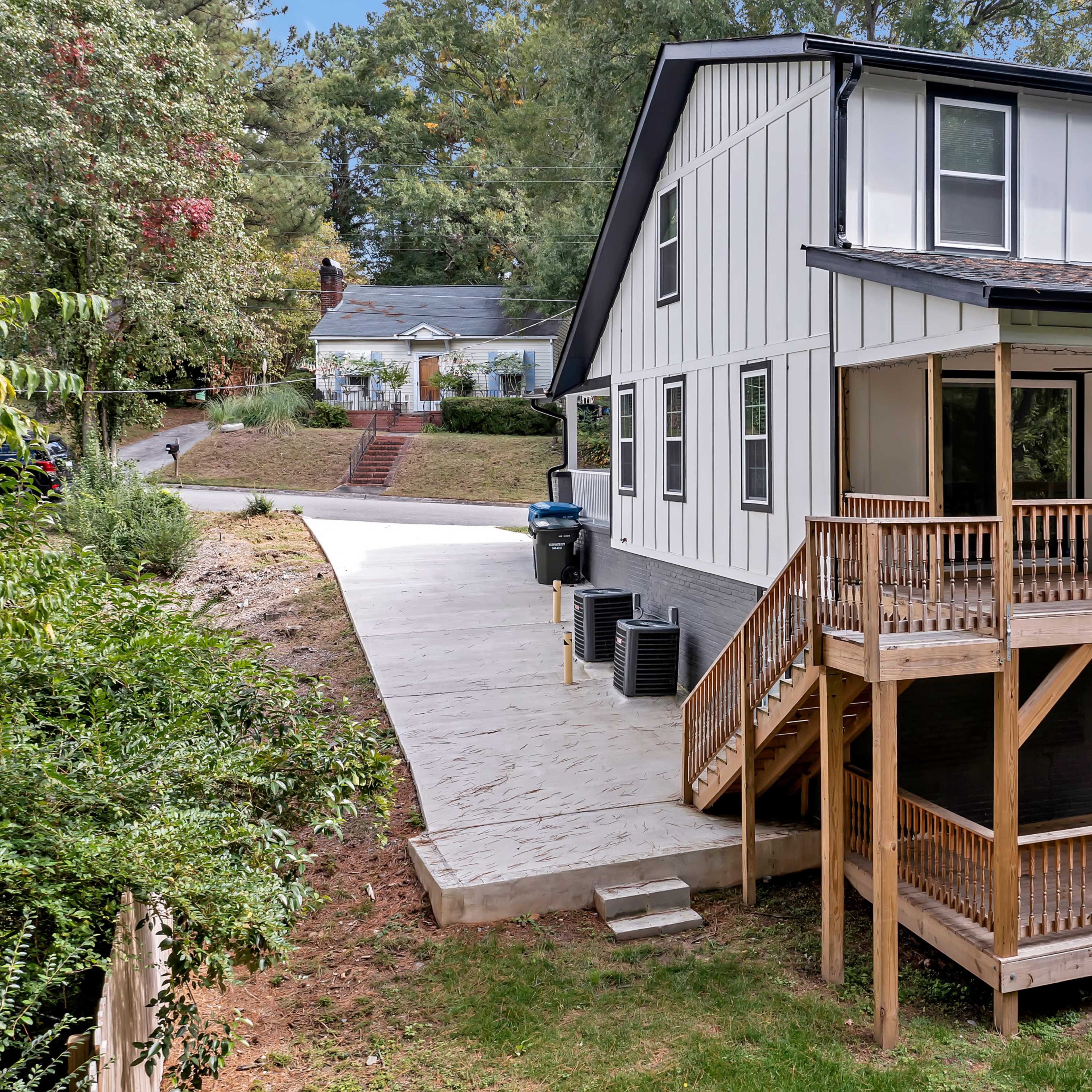 A two-story house with a wooden porch and steps, surrounded by grass and trees, and a driveway leading to the side.