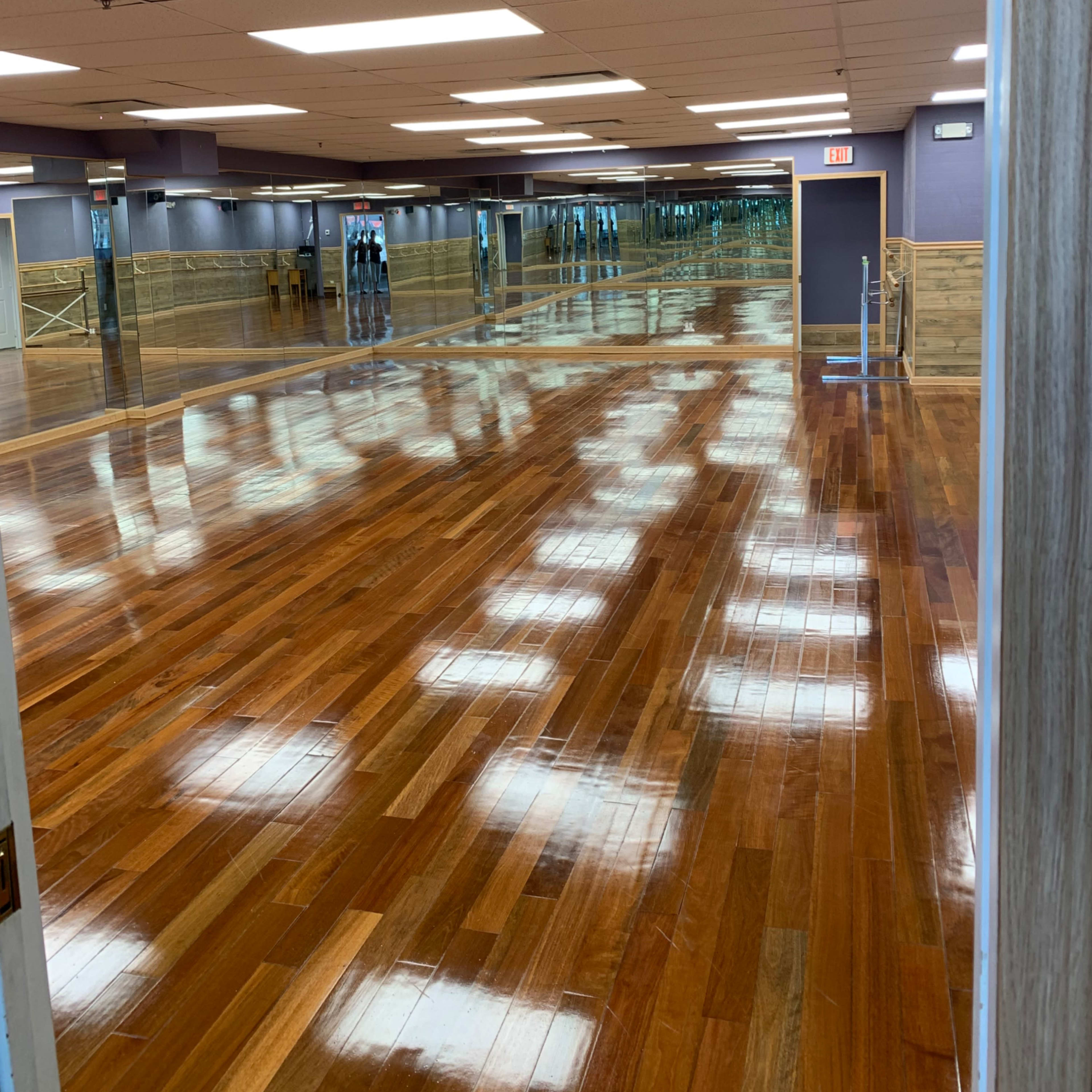 A spacious studio with polished wooden floors and mirrors lining the walls reflects overhead lighting.