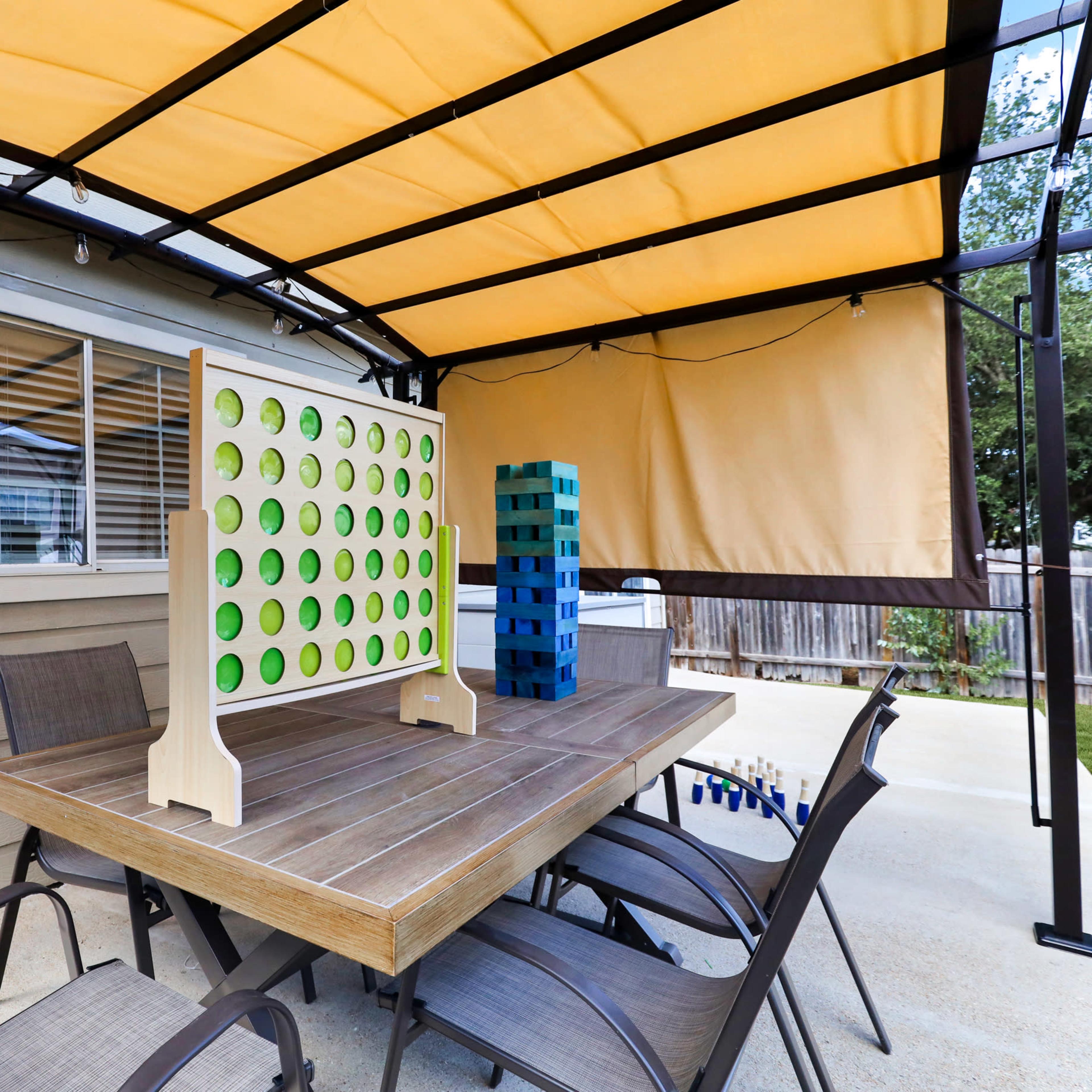 A wooden table with seating under a canopy features a green and blue giant Connect Four game and a stack of colorful blocks.