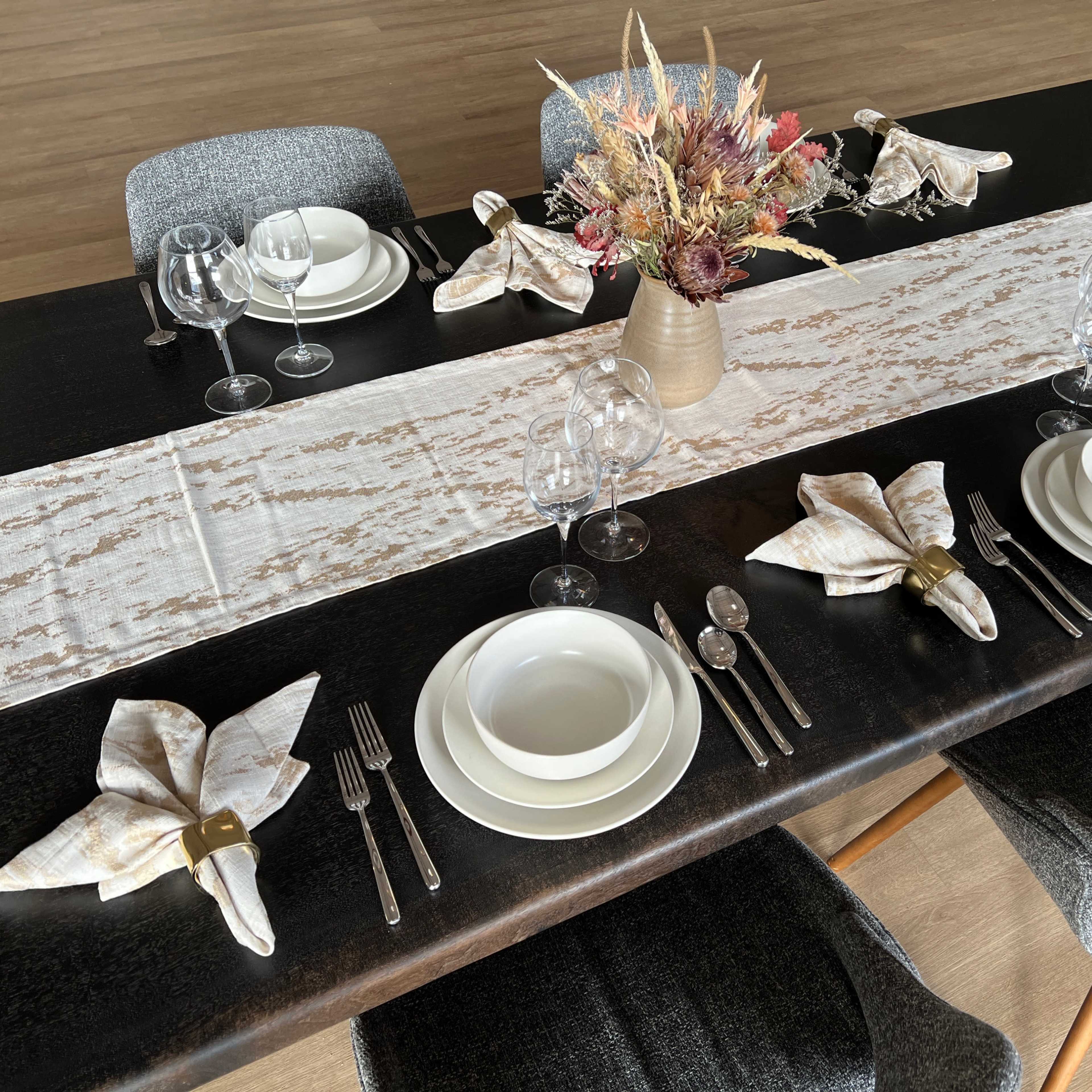A neatly arranged dining table features a table runner, plates, cutlery, glasses, and a floral centerpiece.