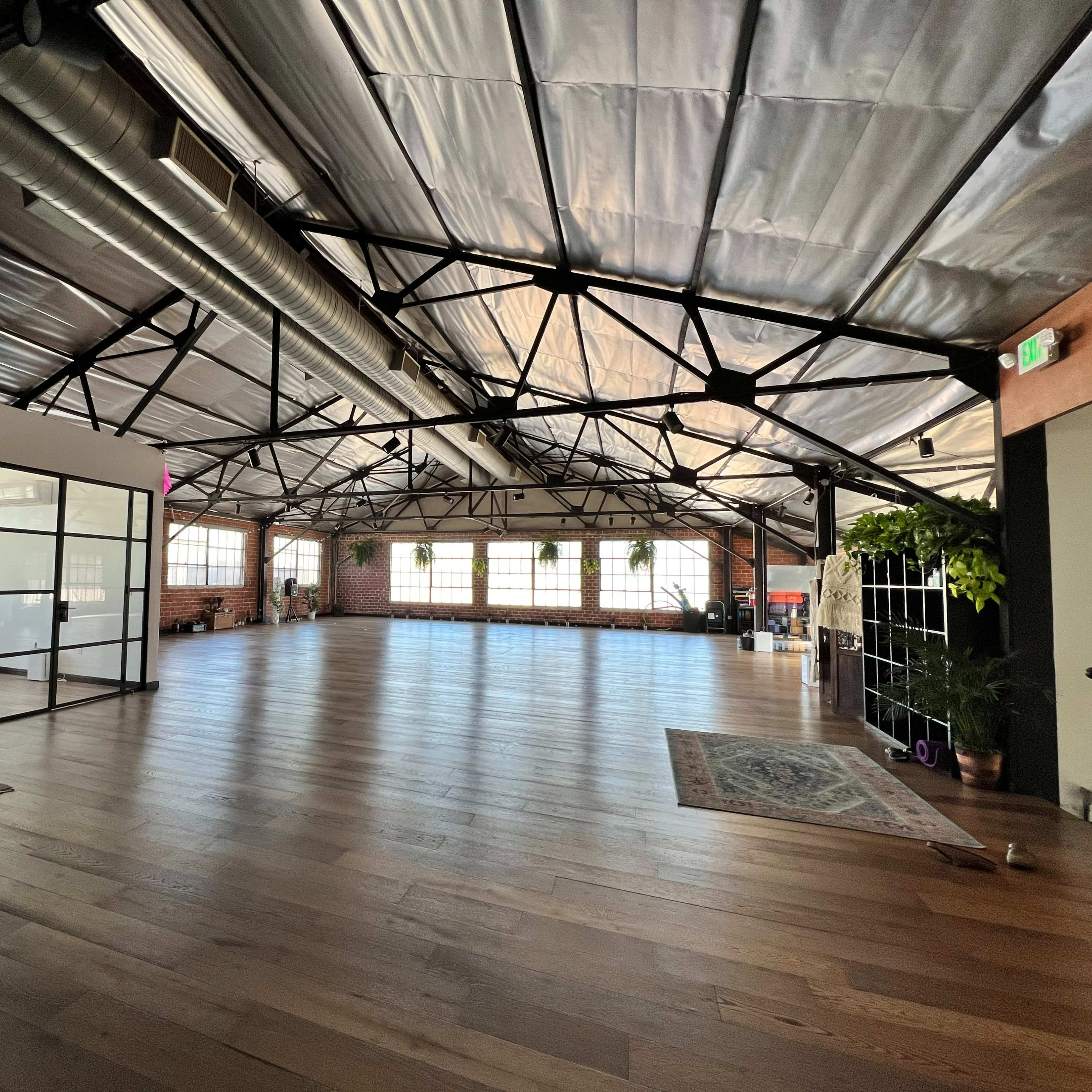 A spacious, industrial-style interior with wooden flooring, large windows, and exposed metal beams.