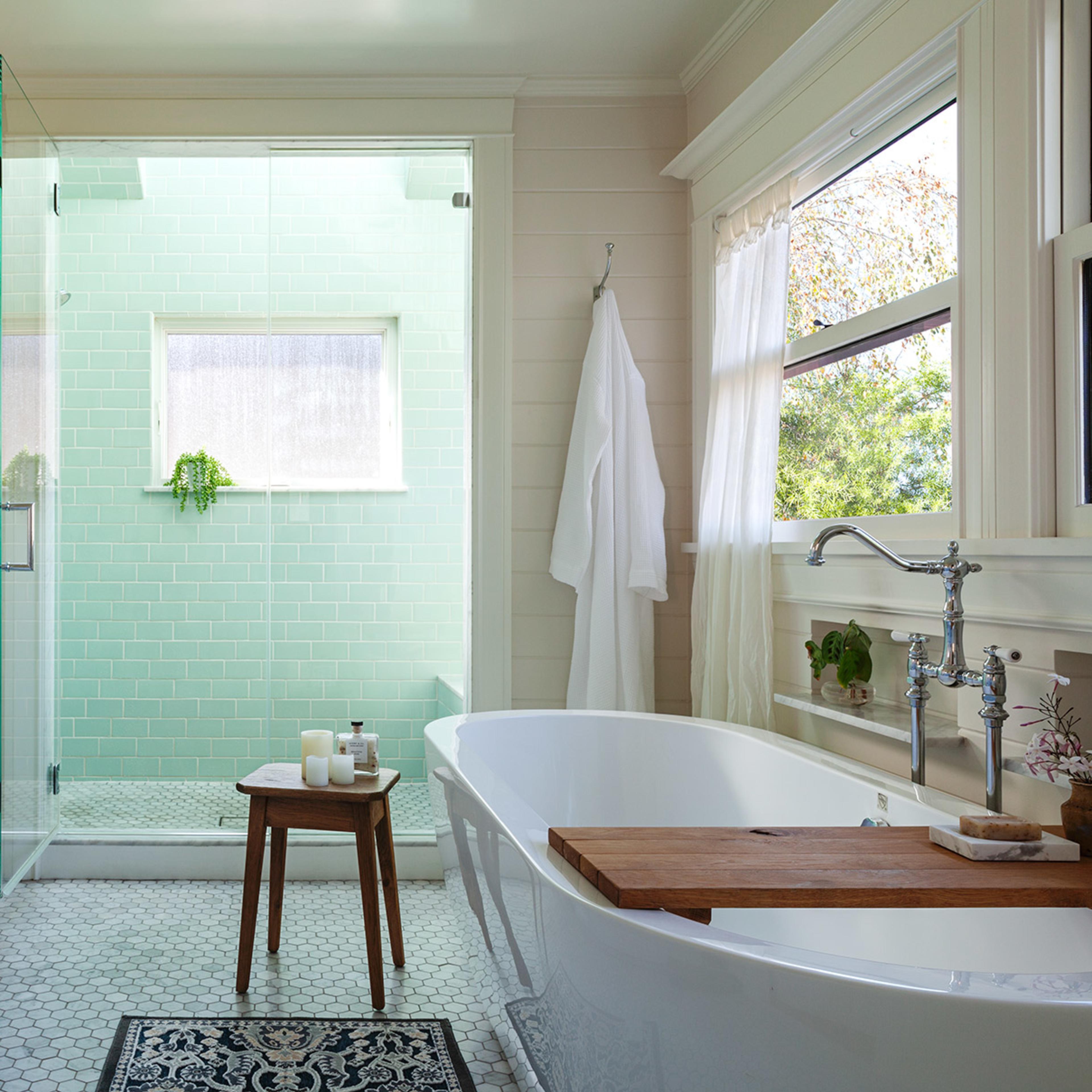 A modern bathroom featuring a freestanding bathtub, a walk-in shower with green tiles, and a double vanity with a marble countertop.