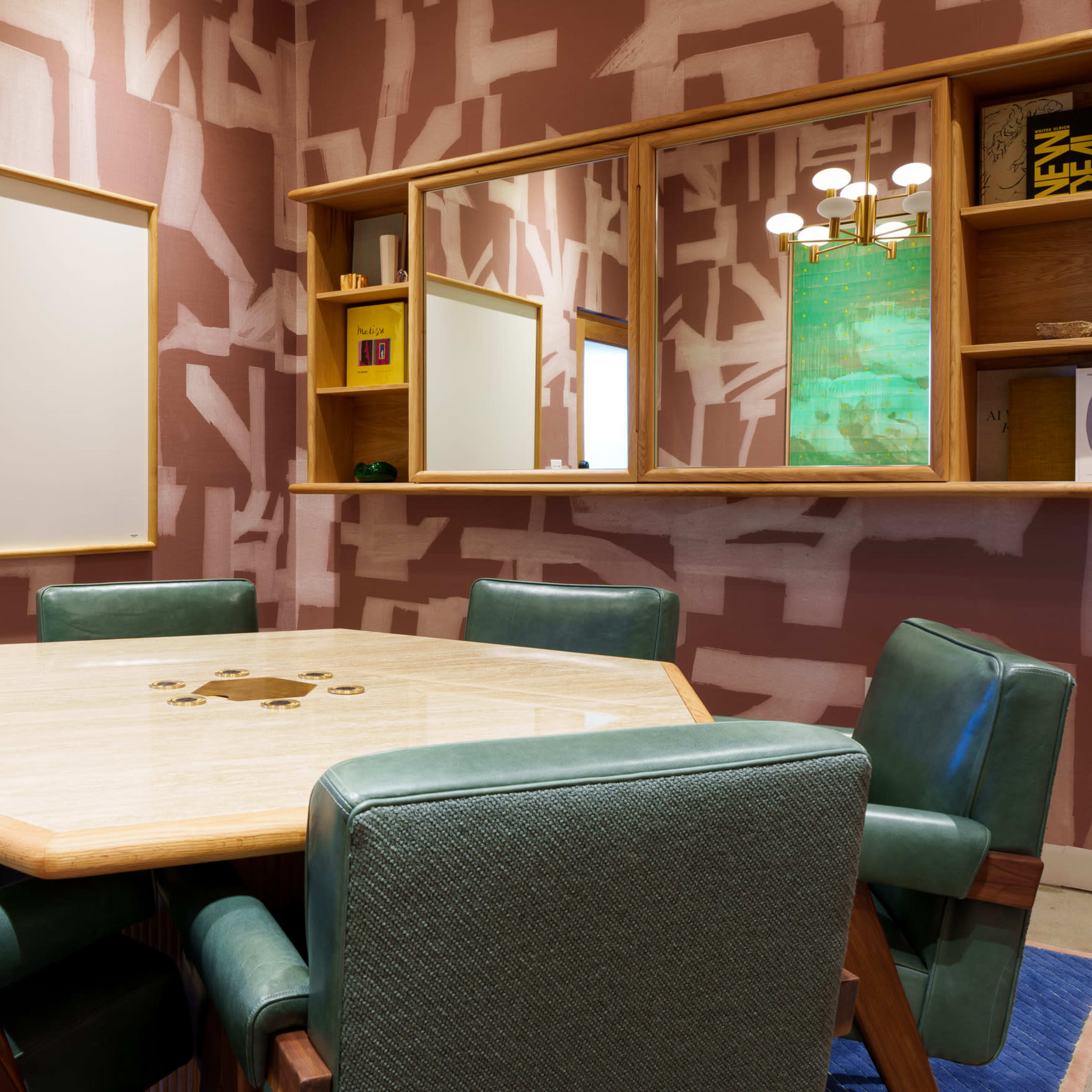 A well-furnished meeting room features a hexagonal table surrounded by green chairs, with a large blank whiteboard and a mirror on the wall.