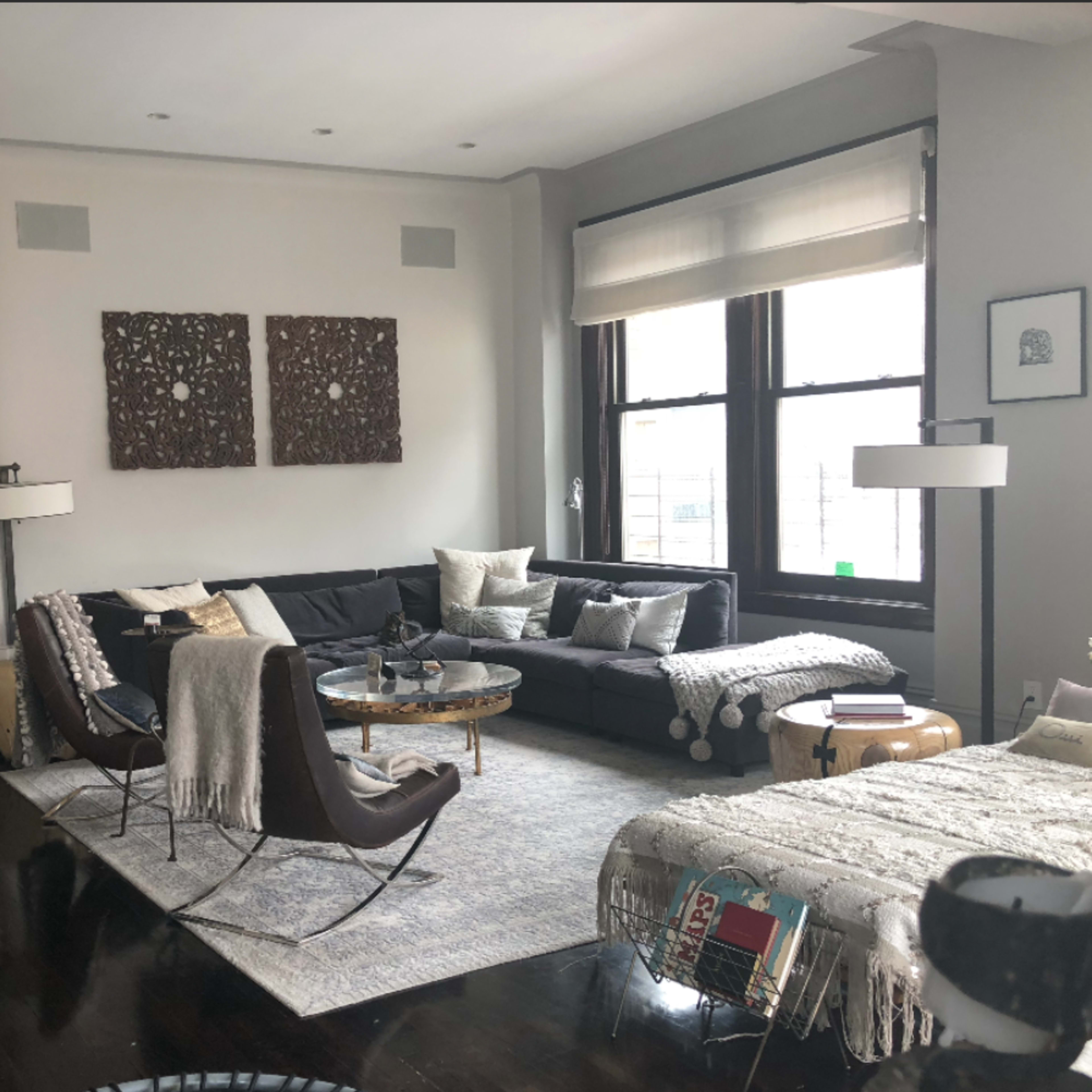 A modern living room features a sectional sofa, a round coffee table, and artwork on the walls, with large windows allowing natural light to enter.