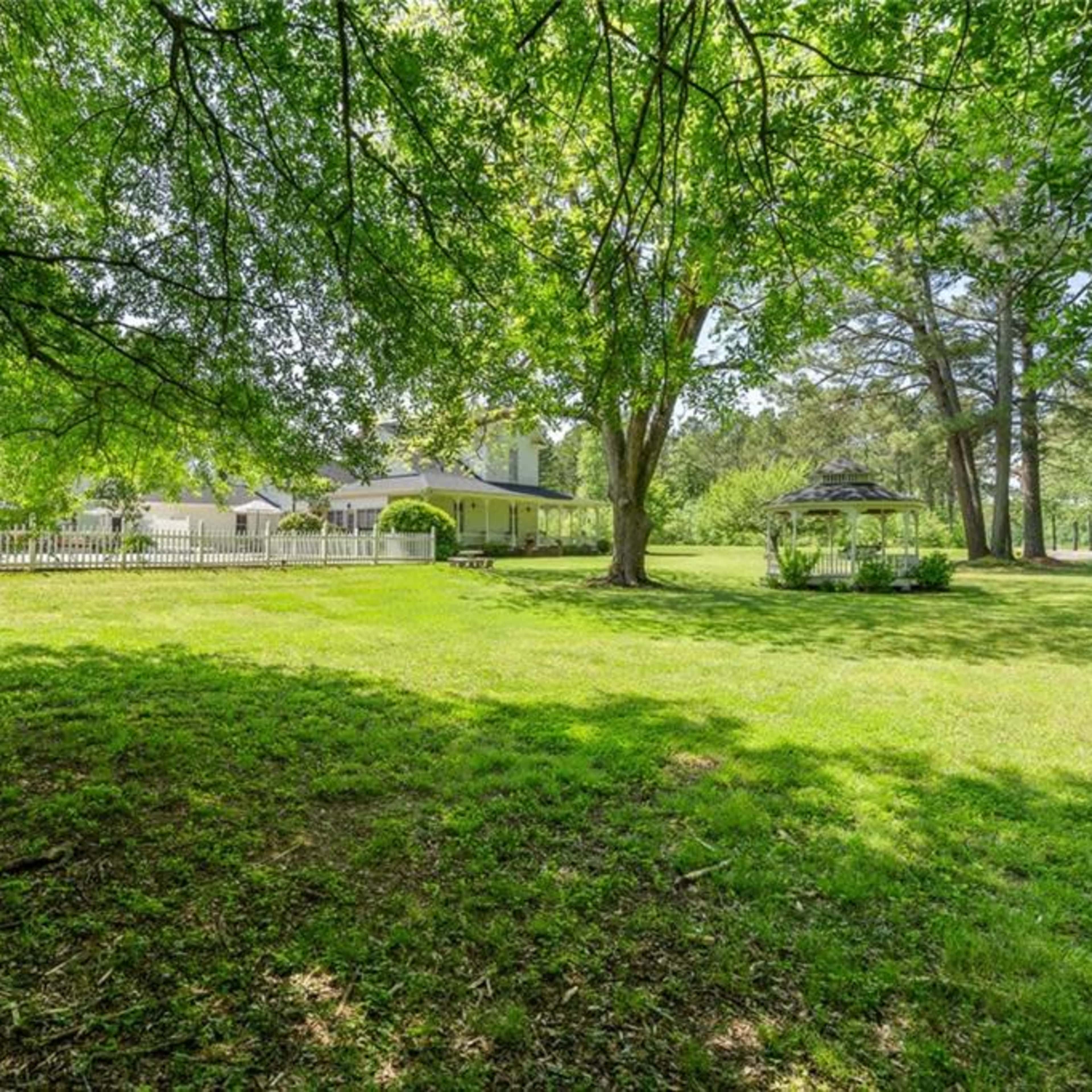 A large, green lawn features a white house and a gazebo surrounded by trees.