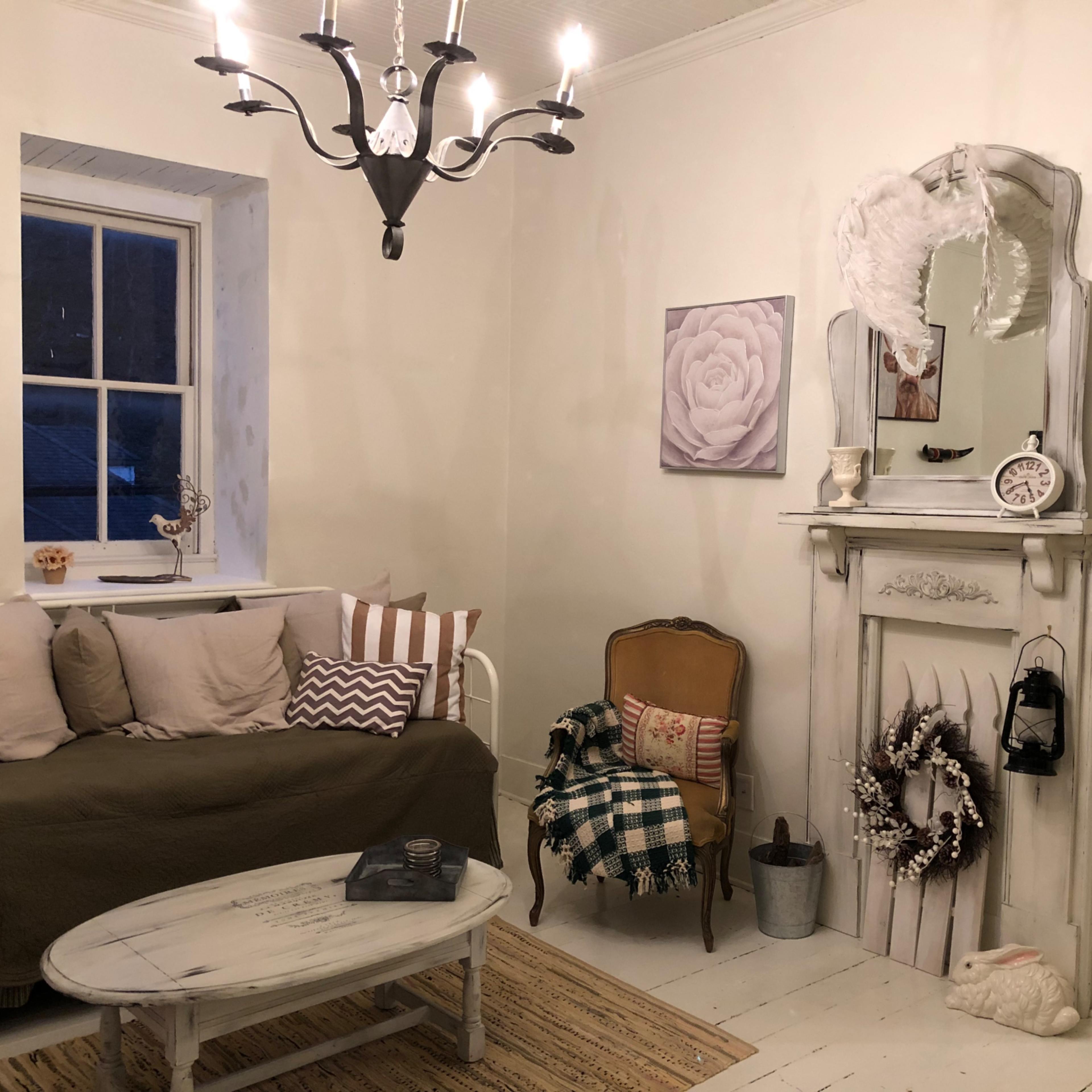 A cozy living room with a light-colored sofa, a decorative mirror above a fireplace, and a chandelier hanging from the ceiling.