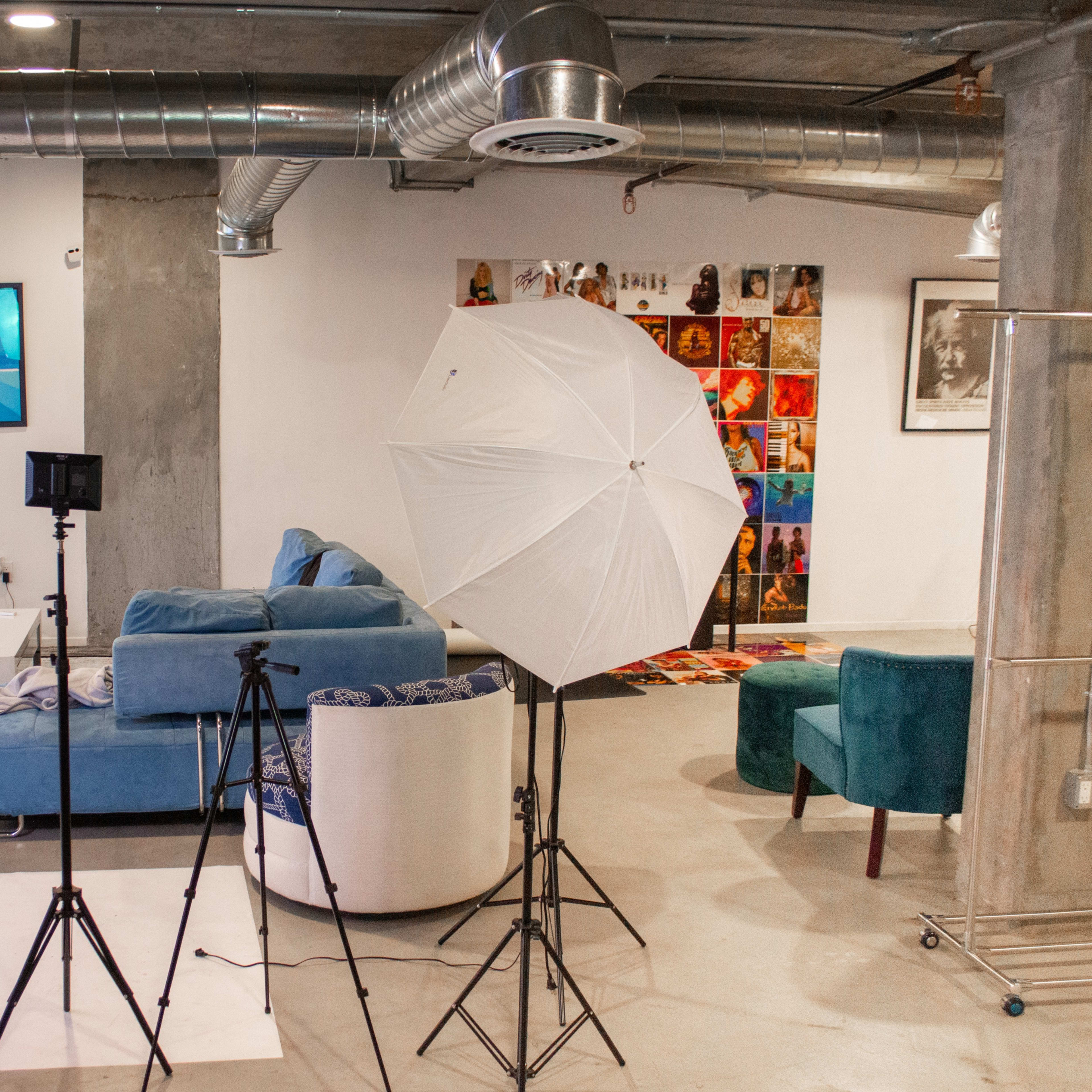 A modern living space with a blue sofa, a television, and various photography equipment set up, including a light umbrella and tripods.