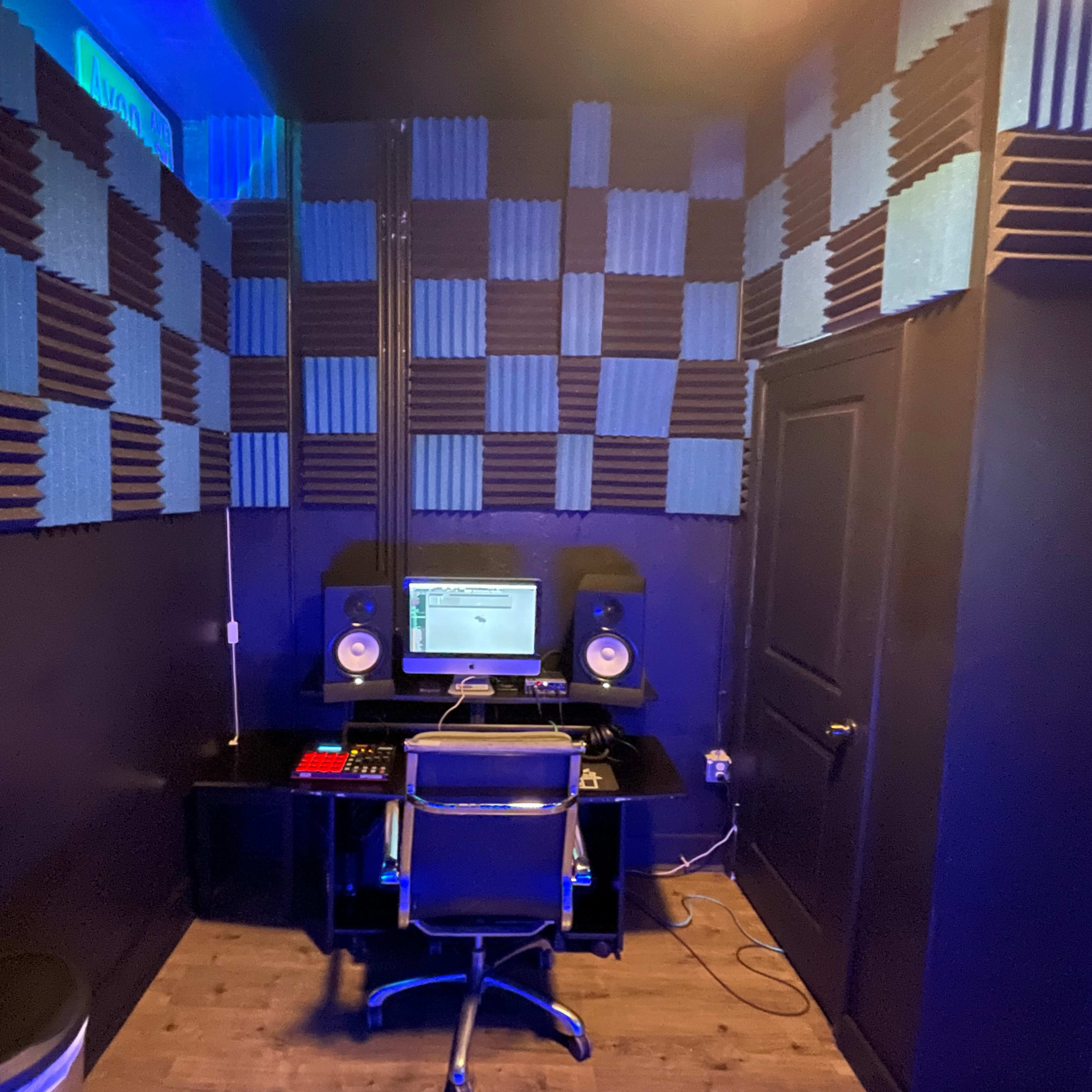 A recording studio with soundproofing panels on the walls, a computer desk, and audio equipment set up in a corner.