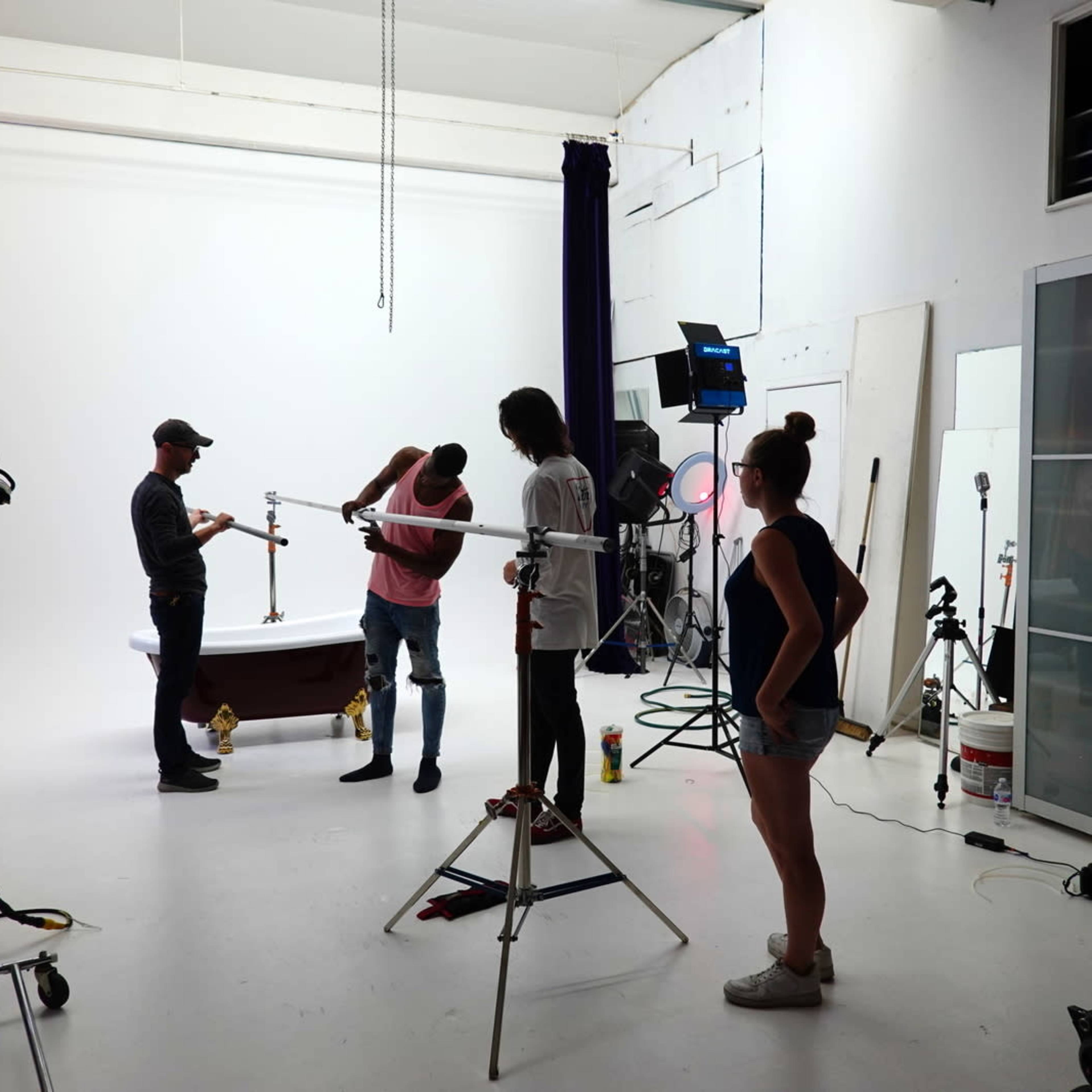 A group of four people is setting up a photography shoot in a studio with a white backdrop and various equipment.