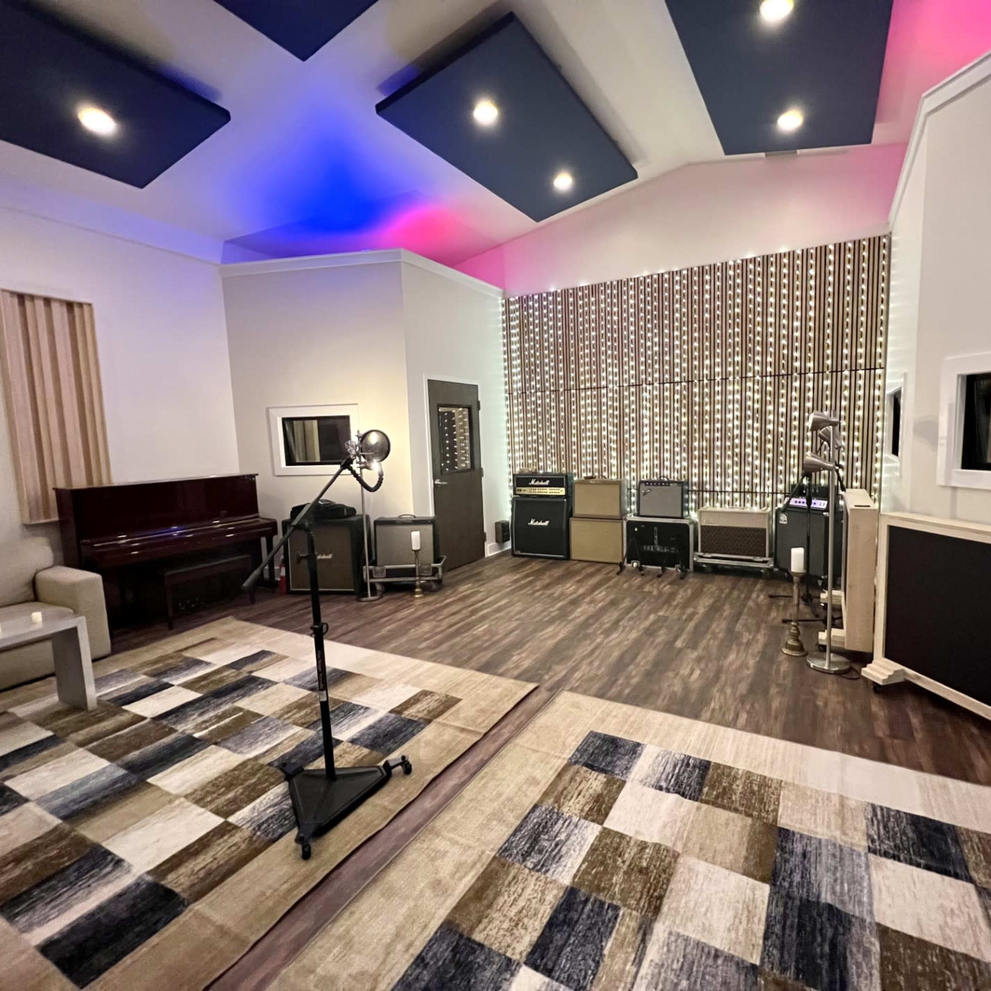A well-equipped recording studio featuring multiple amplifiers, a piano, and a versatile arrangement of rugs and lighting.