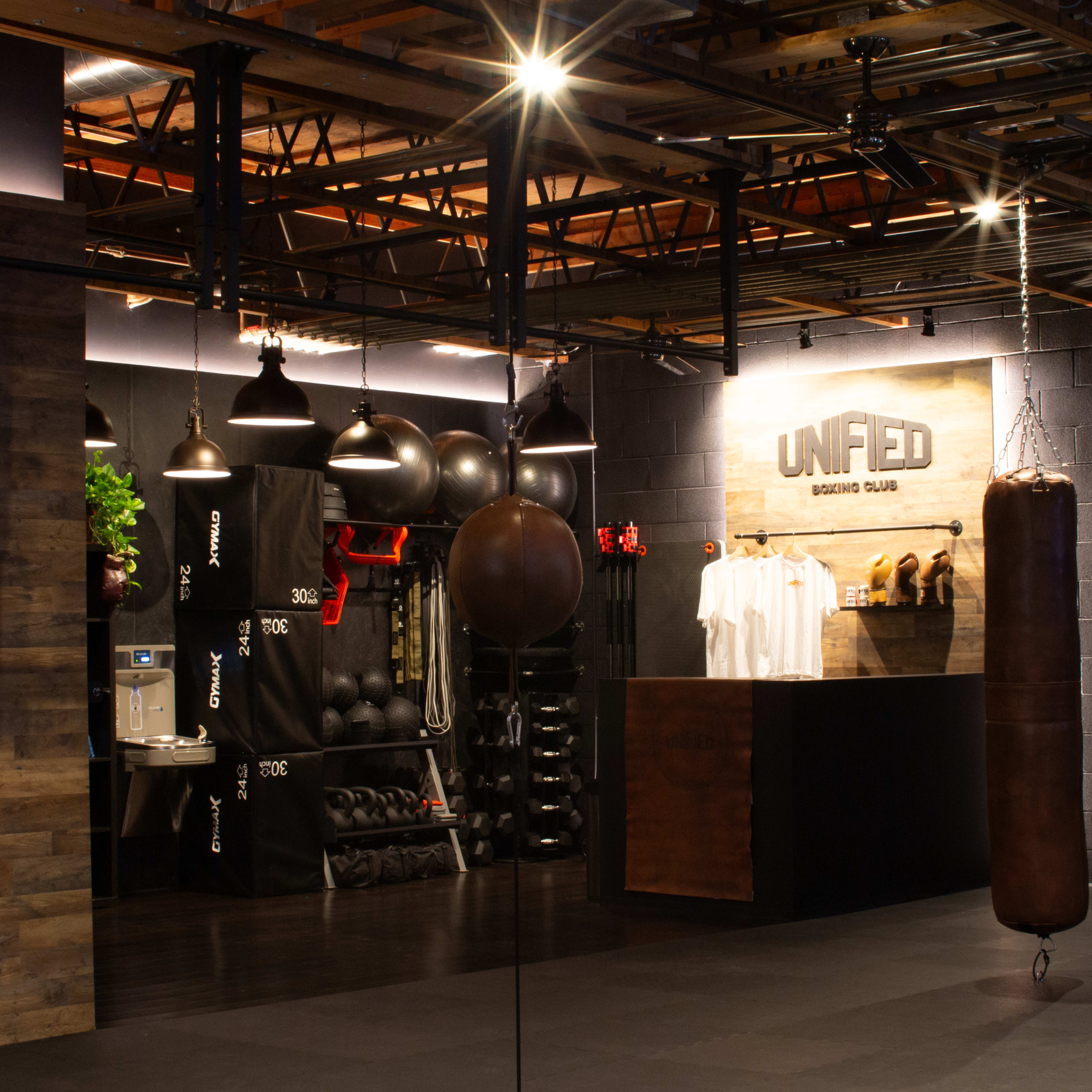 A modern gym interior featuring hanging punching bags and a reception area with branded apparel on display.