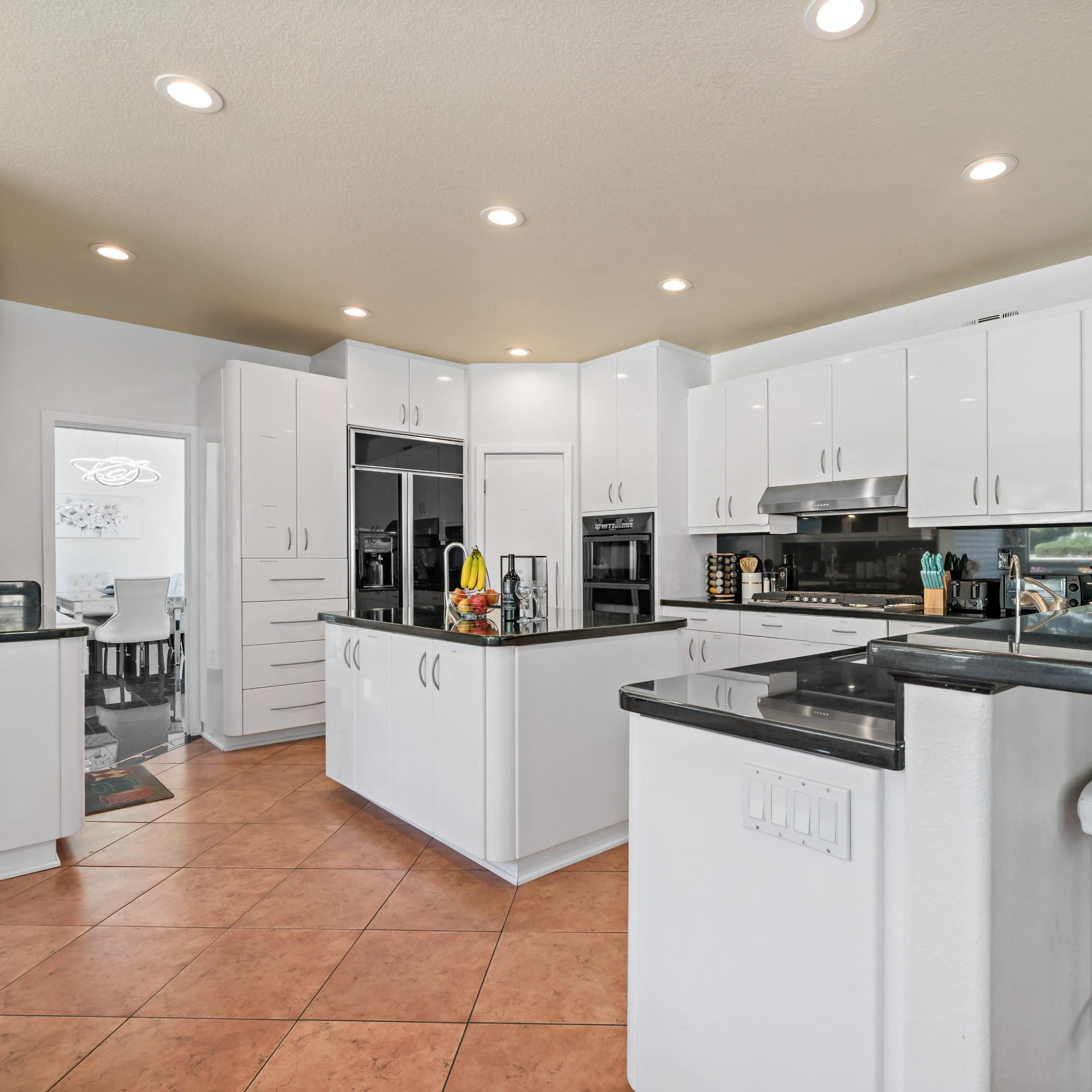 A modern kitchen featuring white cabinetry, black countertops, and a bar with white stools.