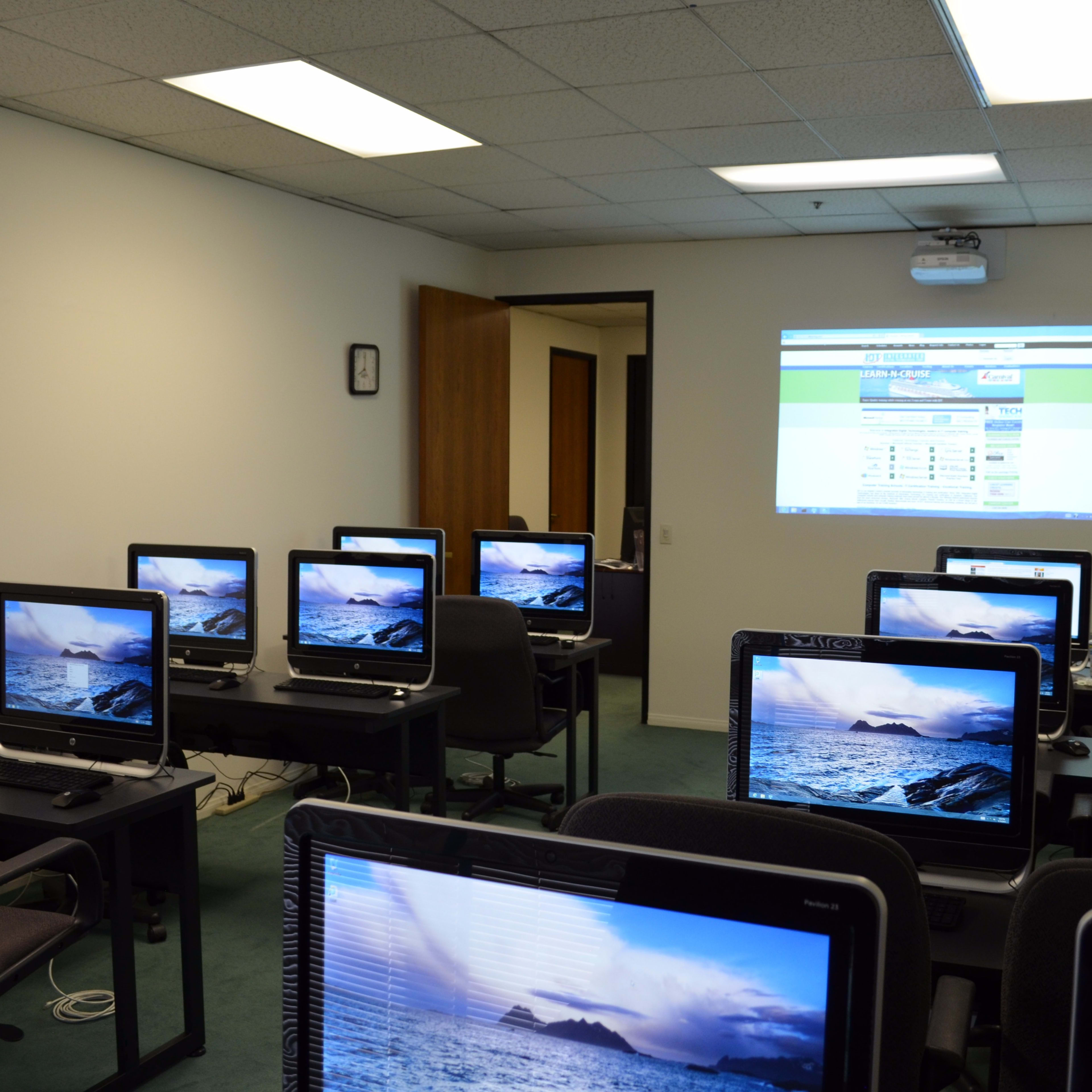 A computer lab with several desktop computers arranged in rows, displaying ocean images, and a projector screen showing a website.
