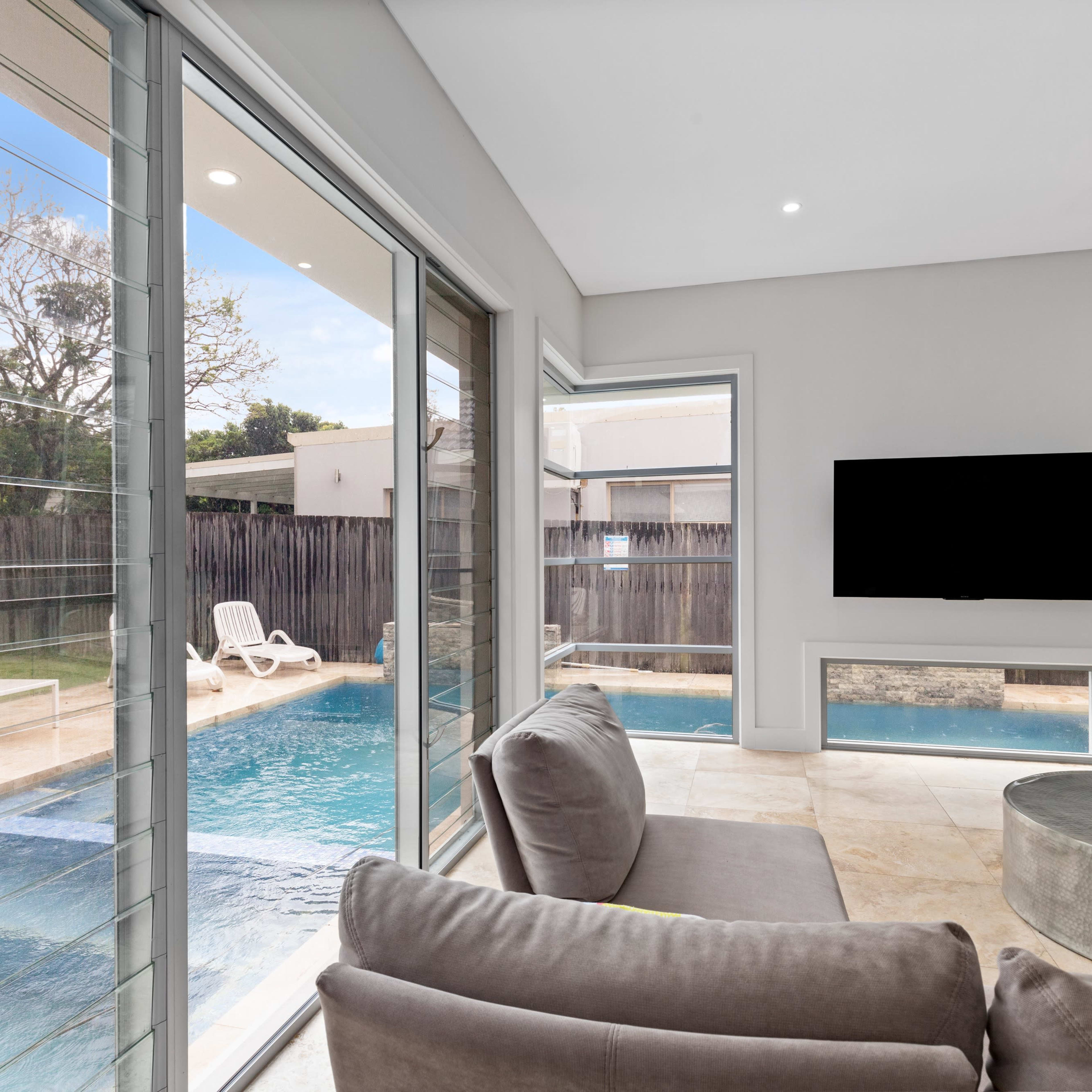 A modern living room with large windows overlooks a swimming pool and backyard area.