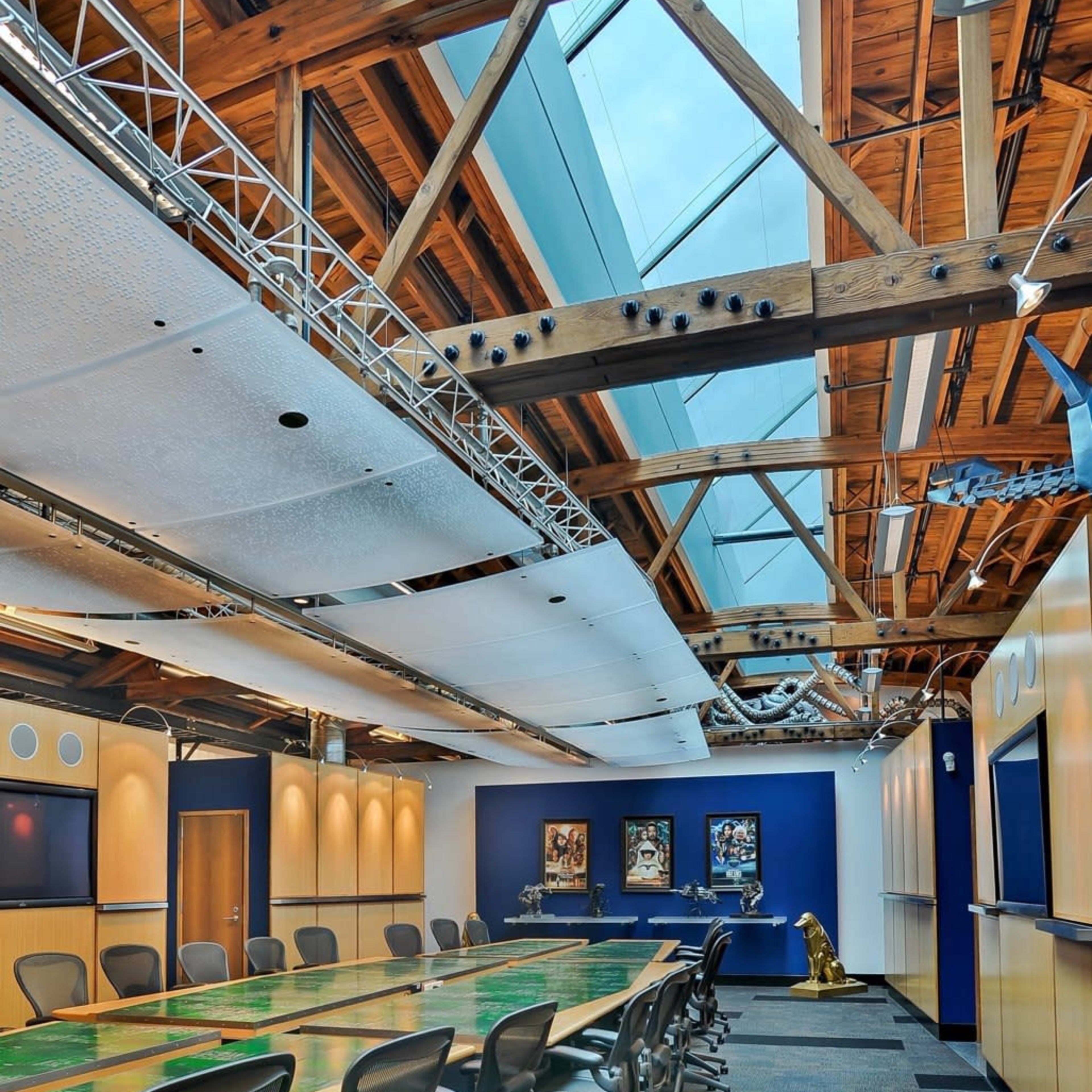 A spacious conference room features a long wooden table surrounded by ergonomic chairs, with exposed wooden beams and a skylight above.