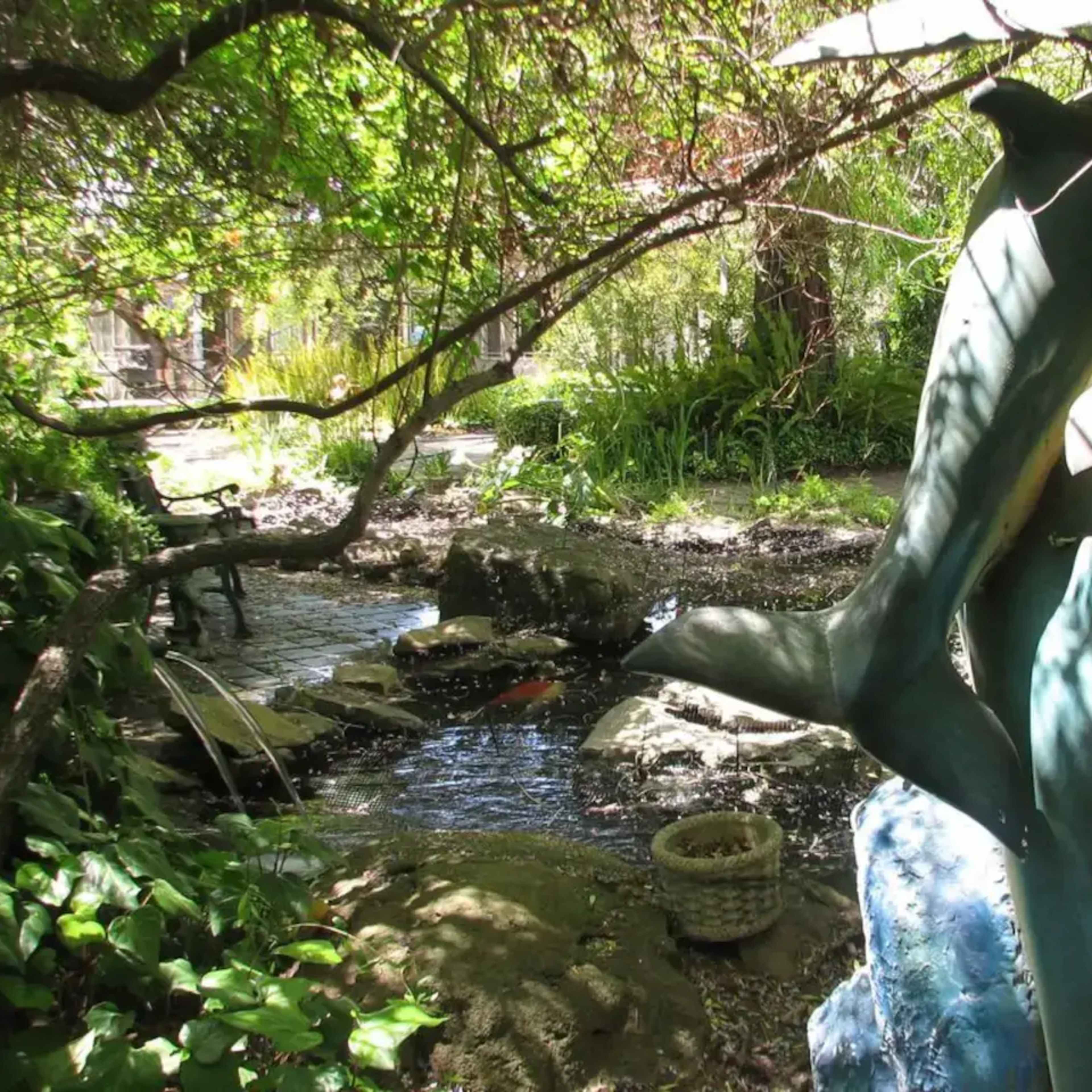 A dolphin sculpture is positioned near a stream surrounded by lush greenery and rocks.
