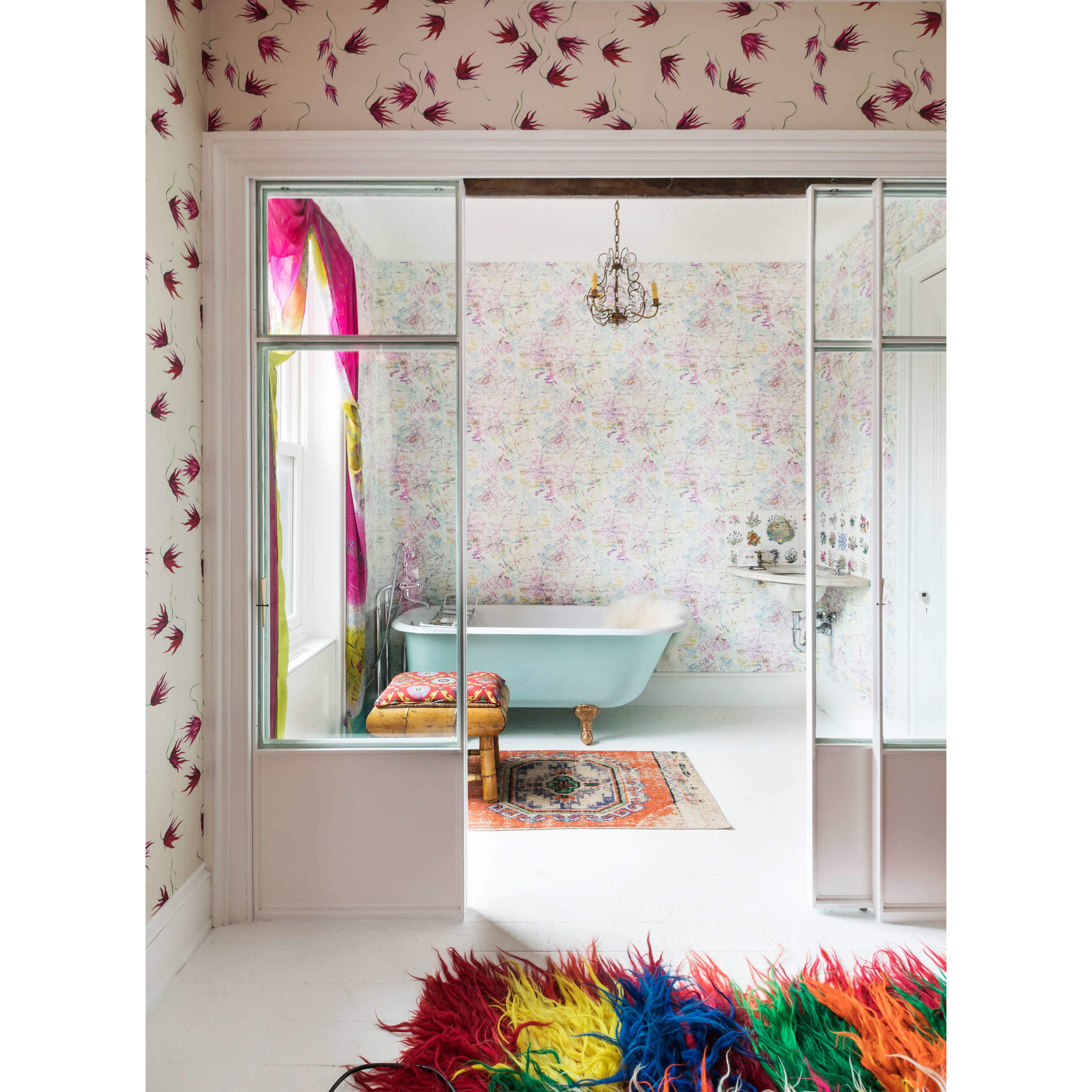 A brightly decorated bathroom featuring a freestanding bathtub, floral wallpaper, and colorful curtains, viewed through an open doorway.