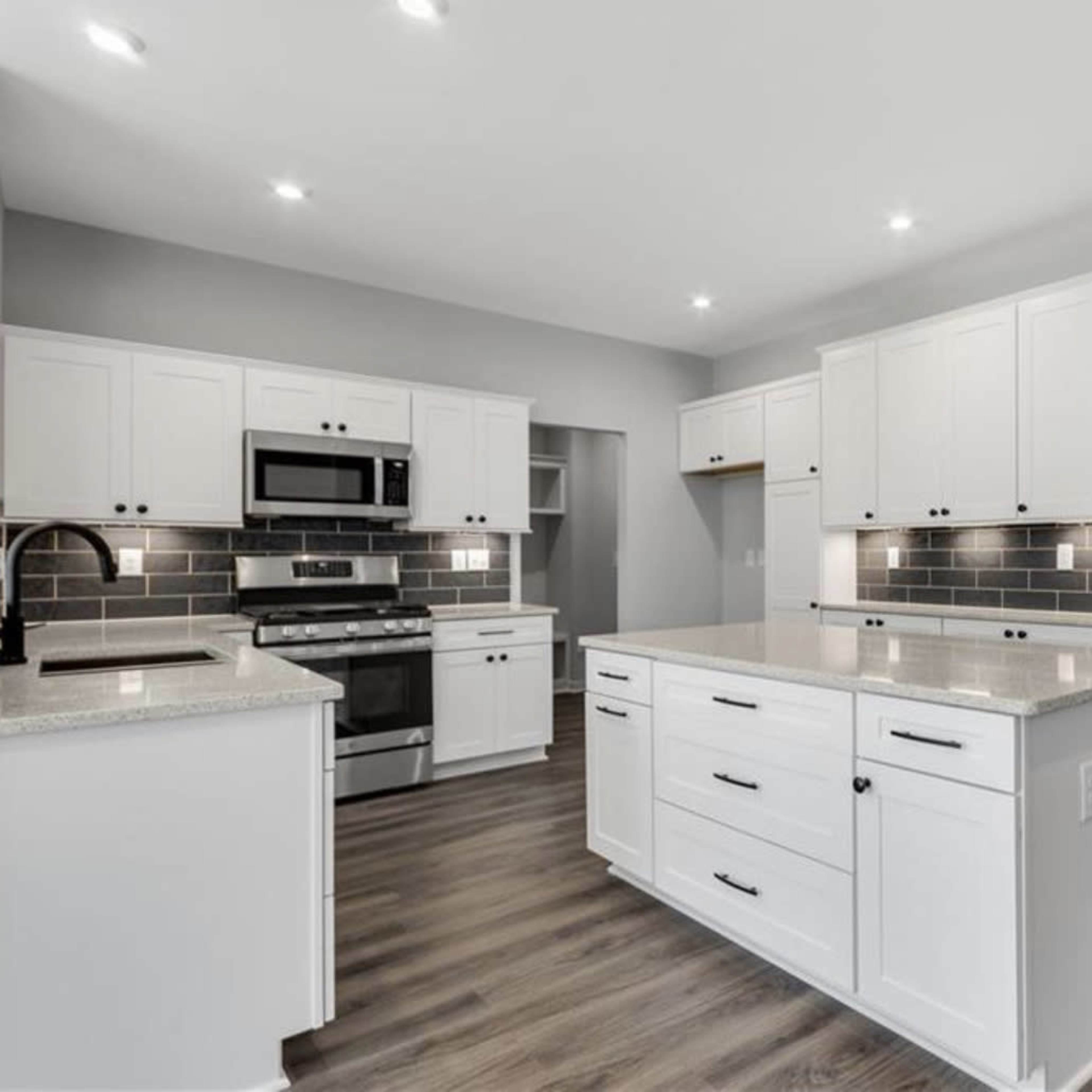 A modern kitchen with white cabinetry, a gray backsplash, and a central island with a countertop.