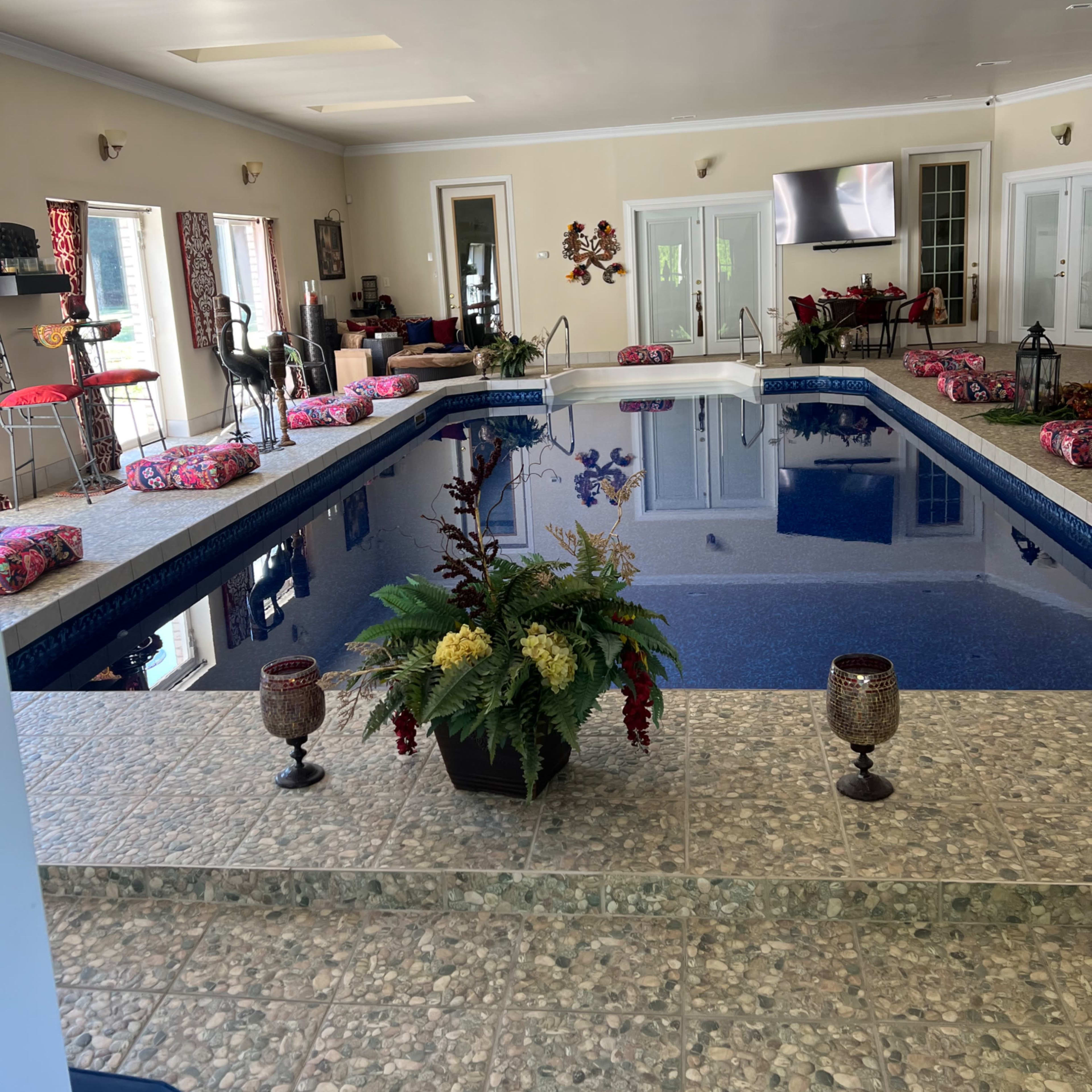 An indoor swimming pool surrounded by decorative plants and seating areas.