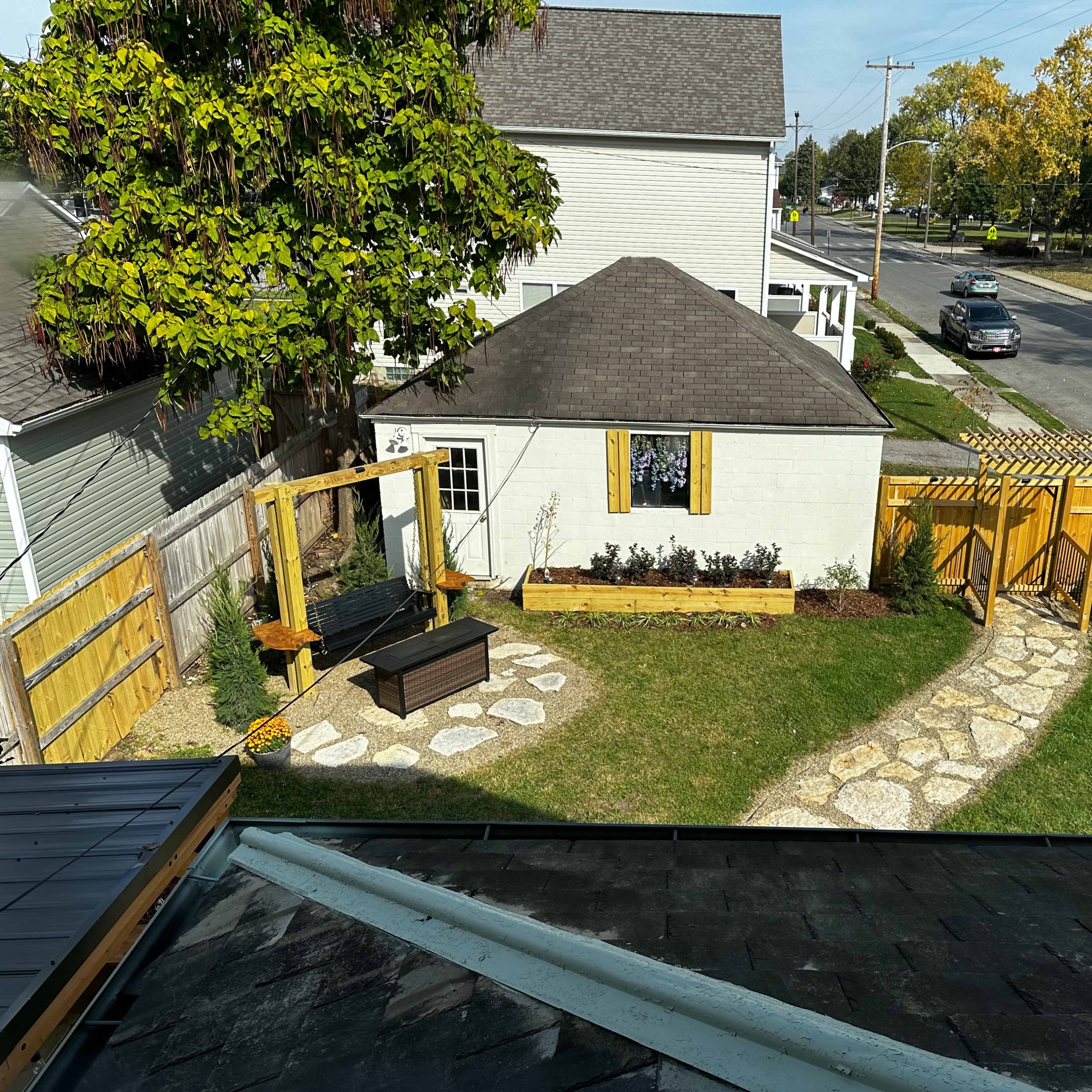 A backyard features a stone pathway leading to a shed, surrounded by a lawn and wooden fences.