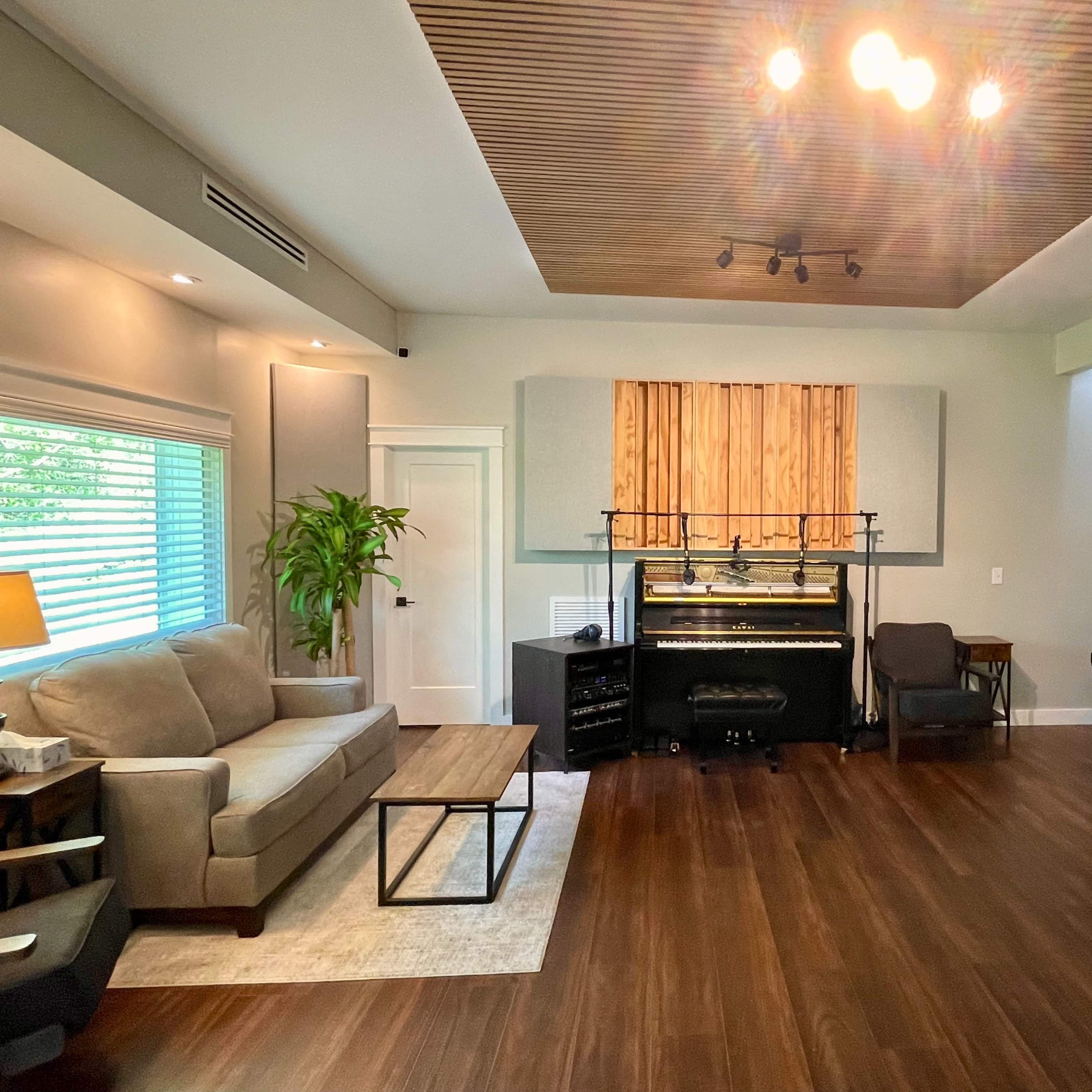 A spacious room features a piano, a couch, a coffee table, and large windows with natural light.