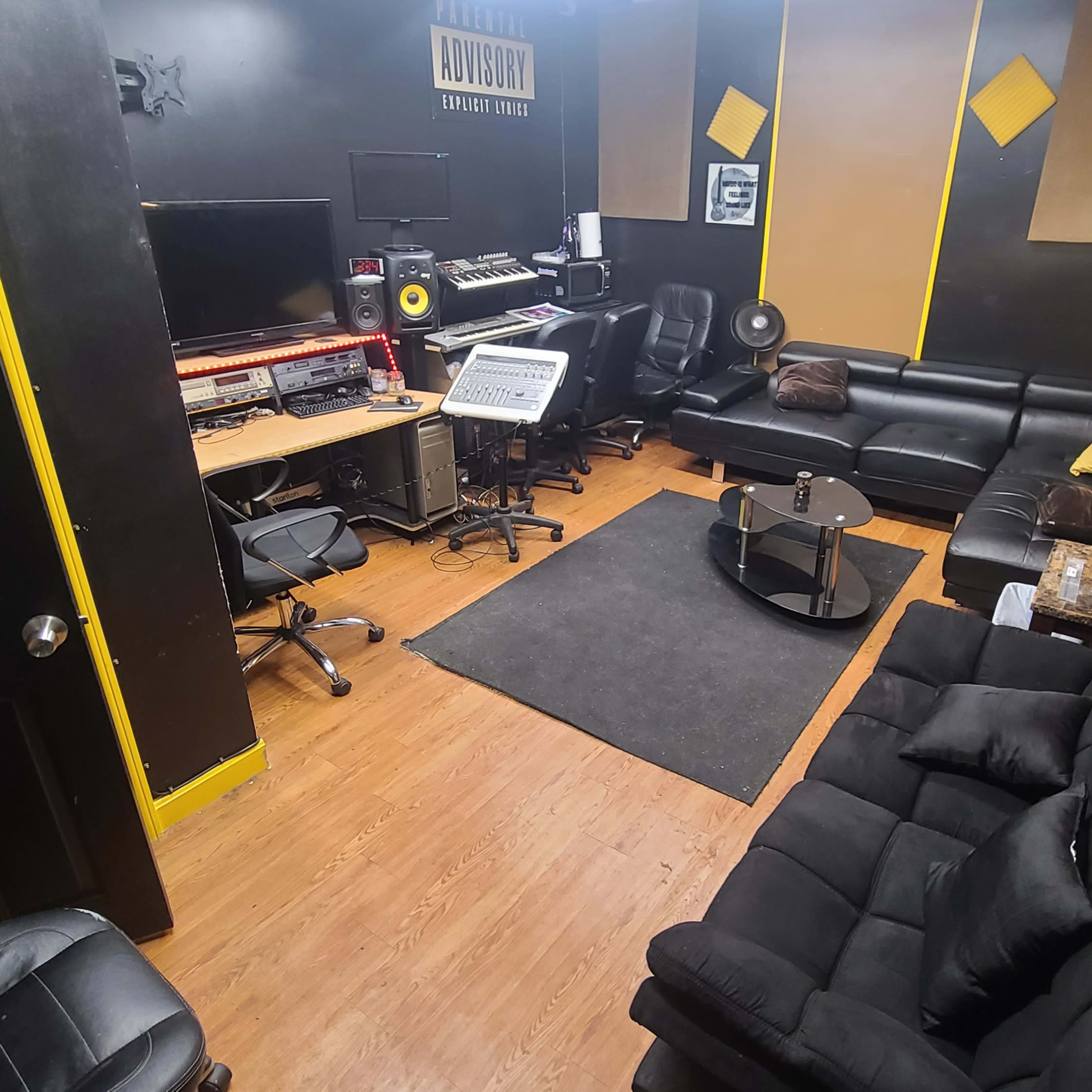 A recording studio with black sofas, a computer workstation, and sound equipment arranged in a compact space.