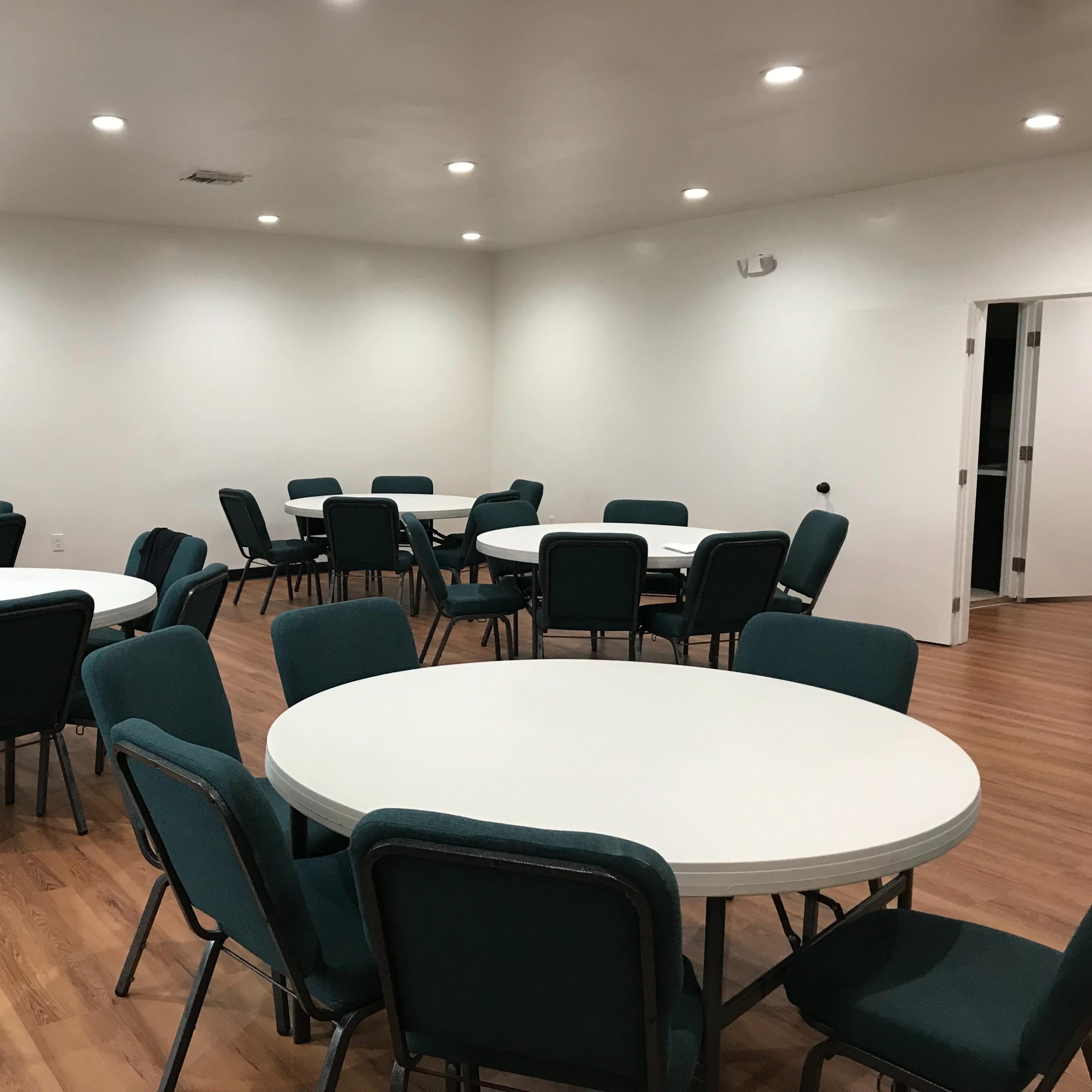 A spacious room with several round tables and chairs arranged around them, set on a wooden floor.
