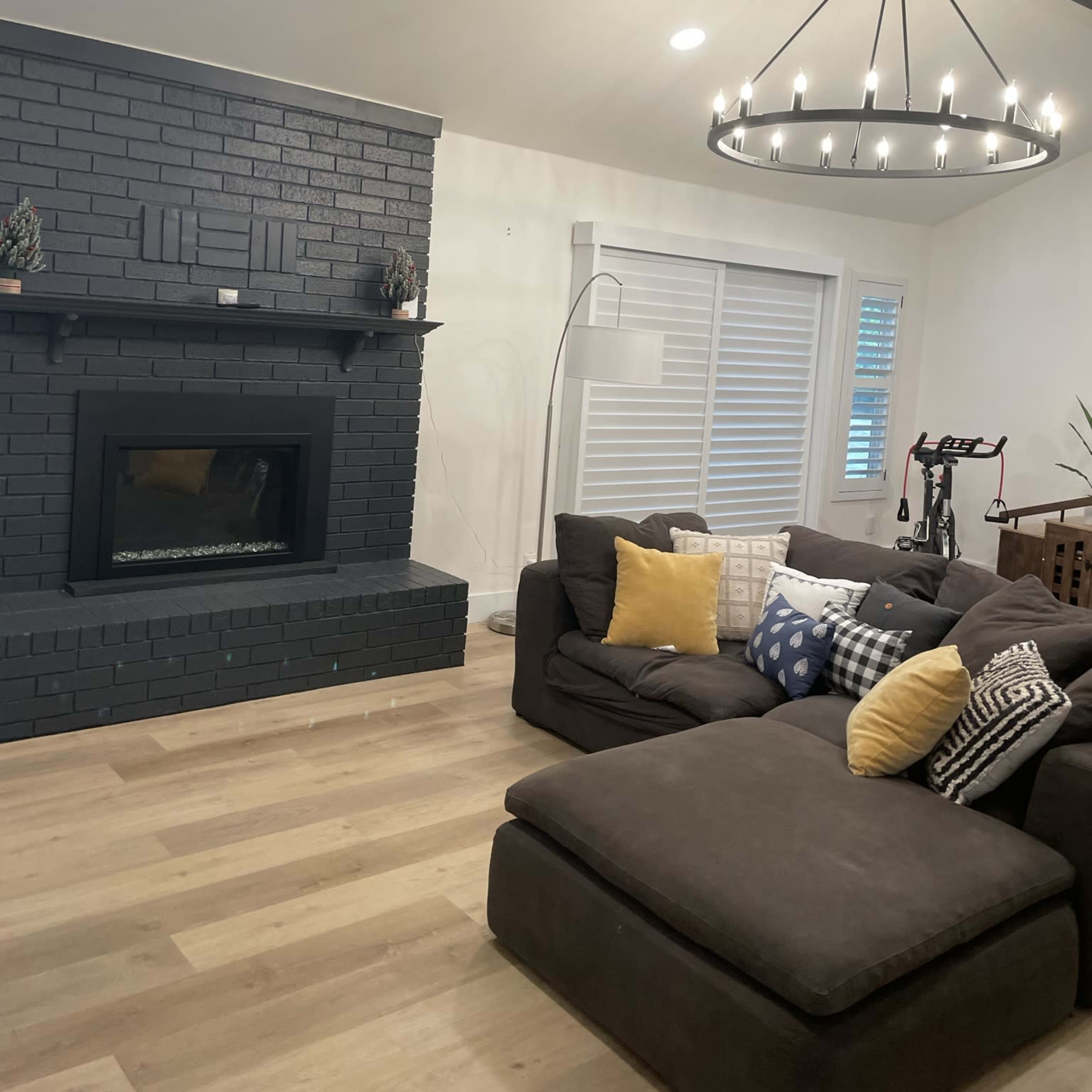 A living room featuring a dark brick fireplace, a large sectional sofa with decorative pillows, and a modern chandelier.