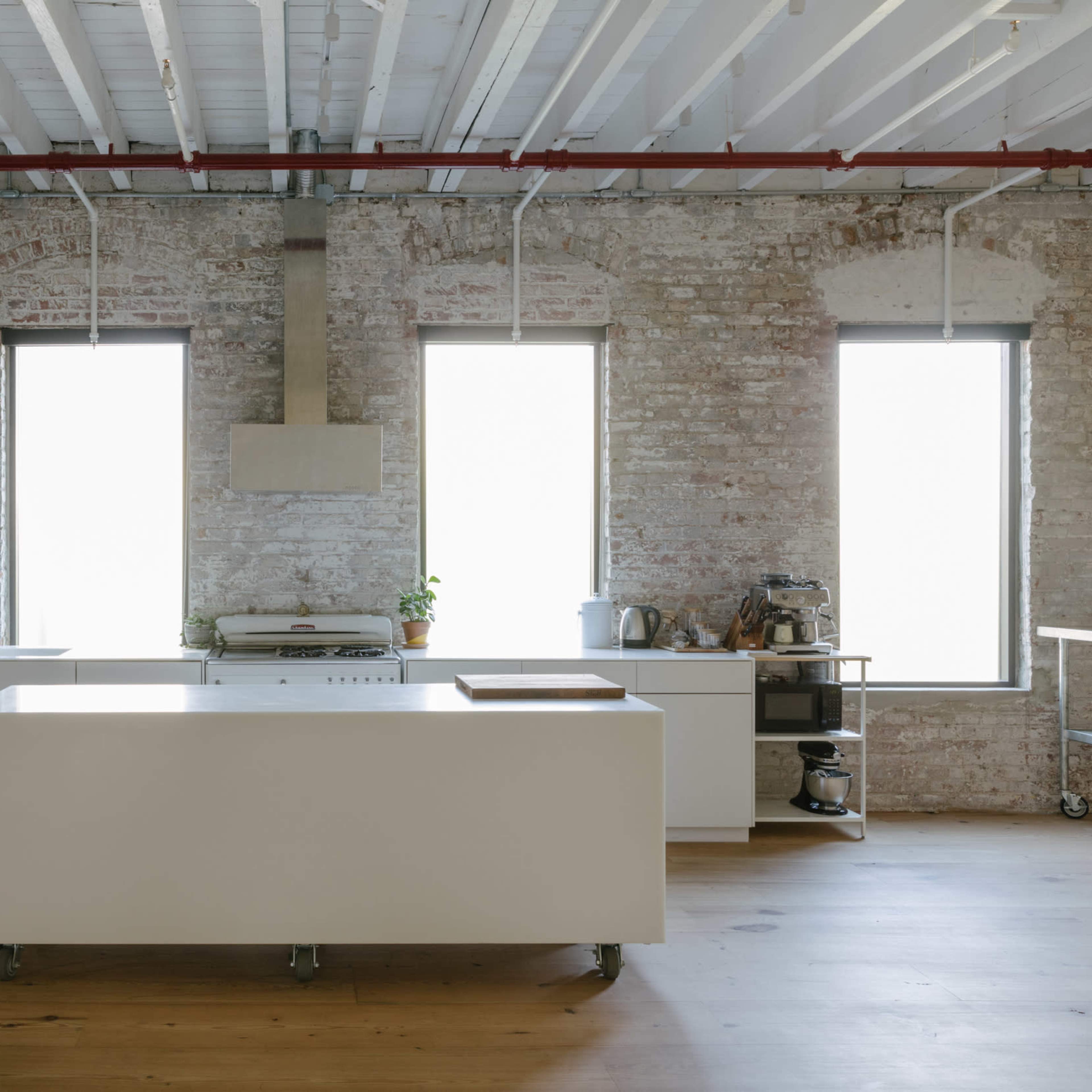 A spacious kitchen with a central island, exposed brick walls, and large windows allowing natural light to fill the room.