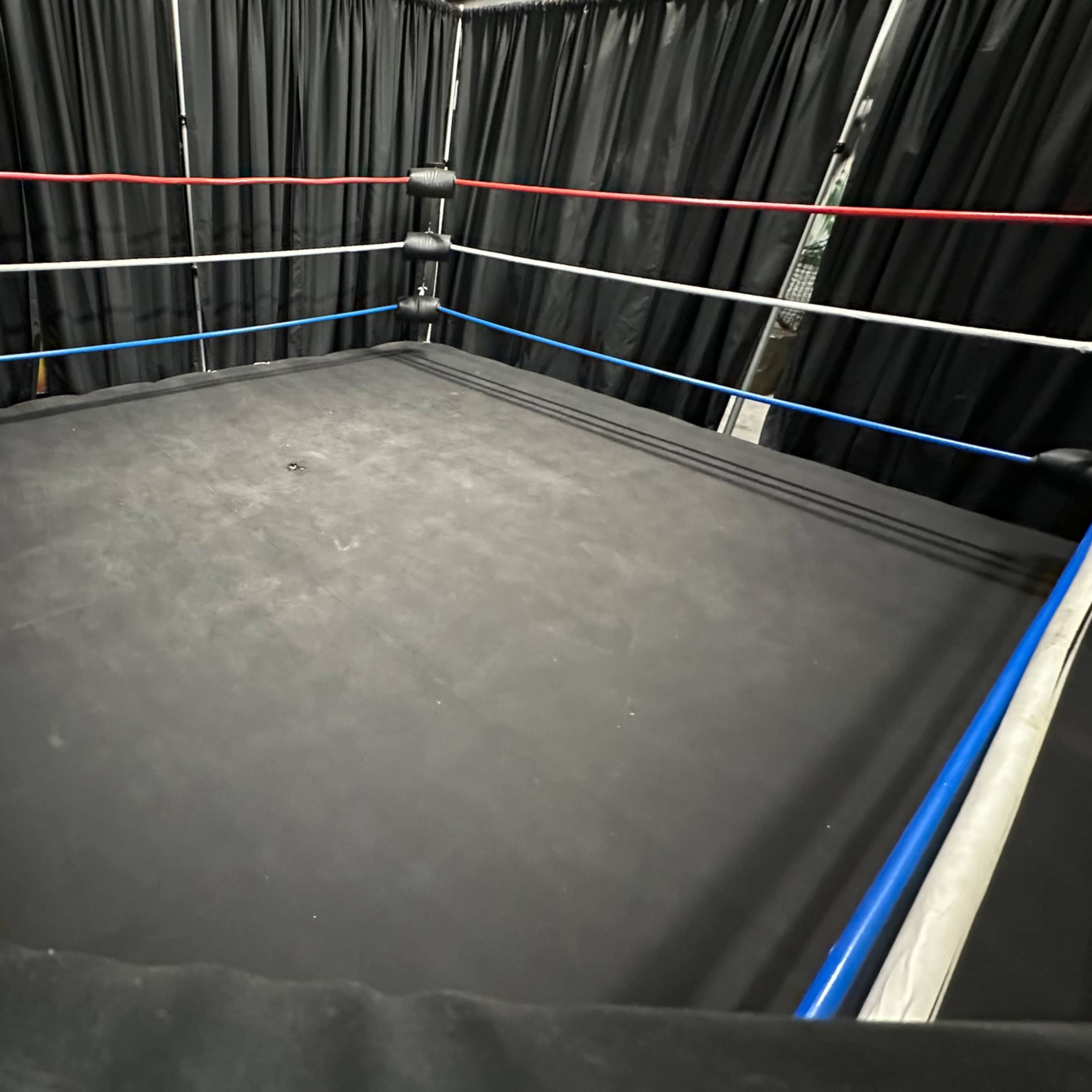 An empty boxing ring surrounded by black curtains with red, white, and blue ropes.