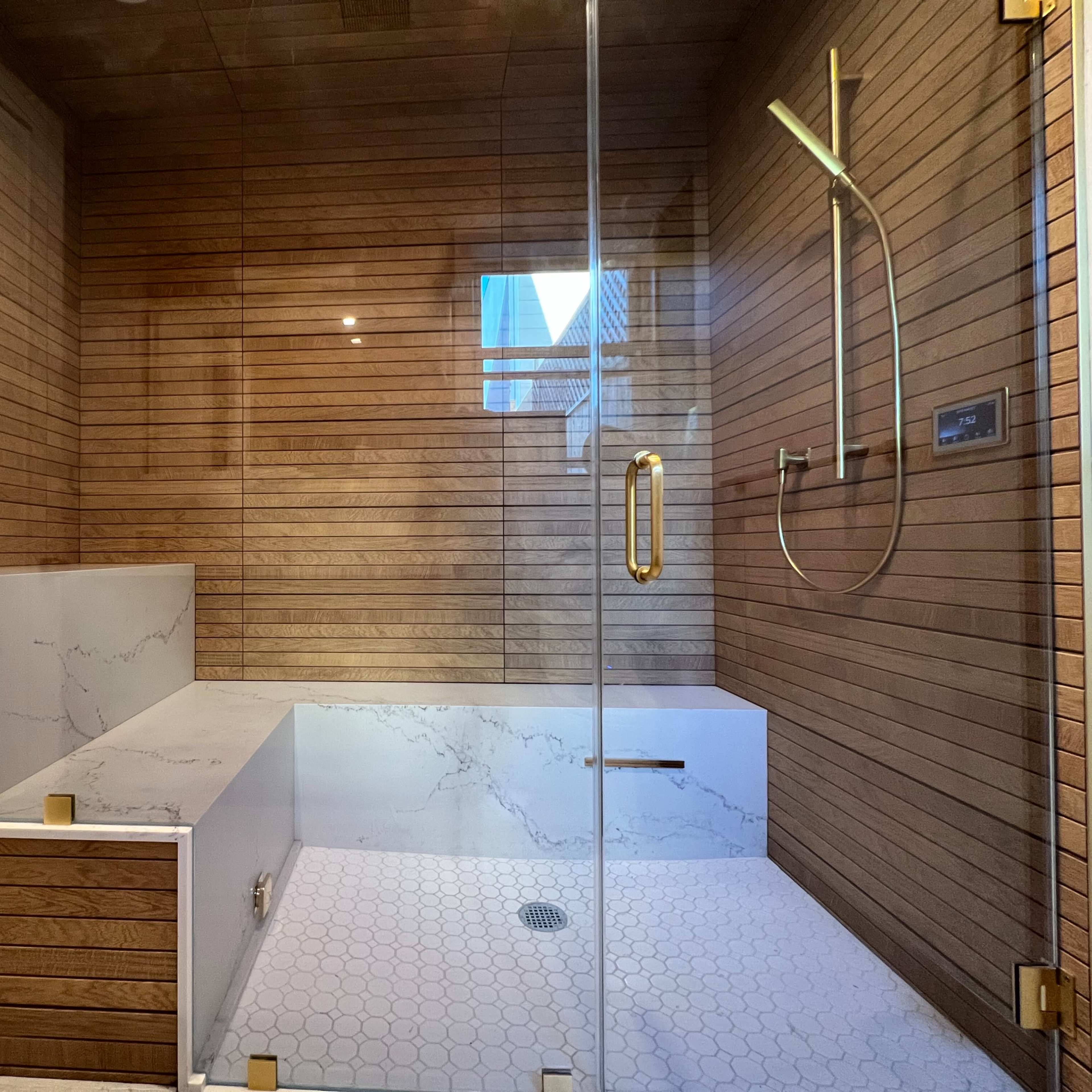 A modern shower with wooden paneling, a marble bench, and a glass enclosure.