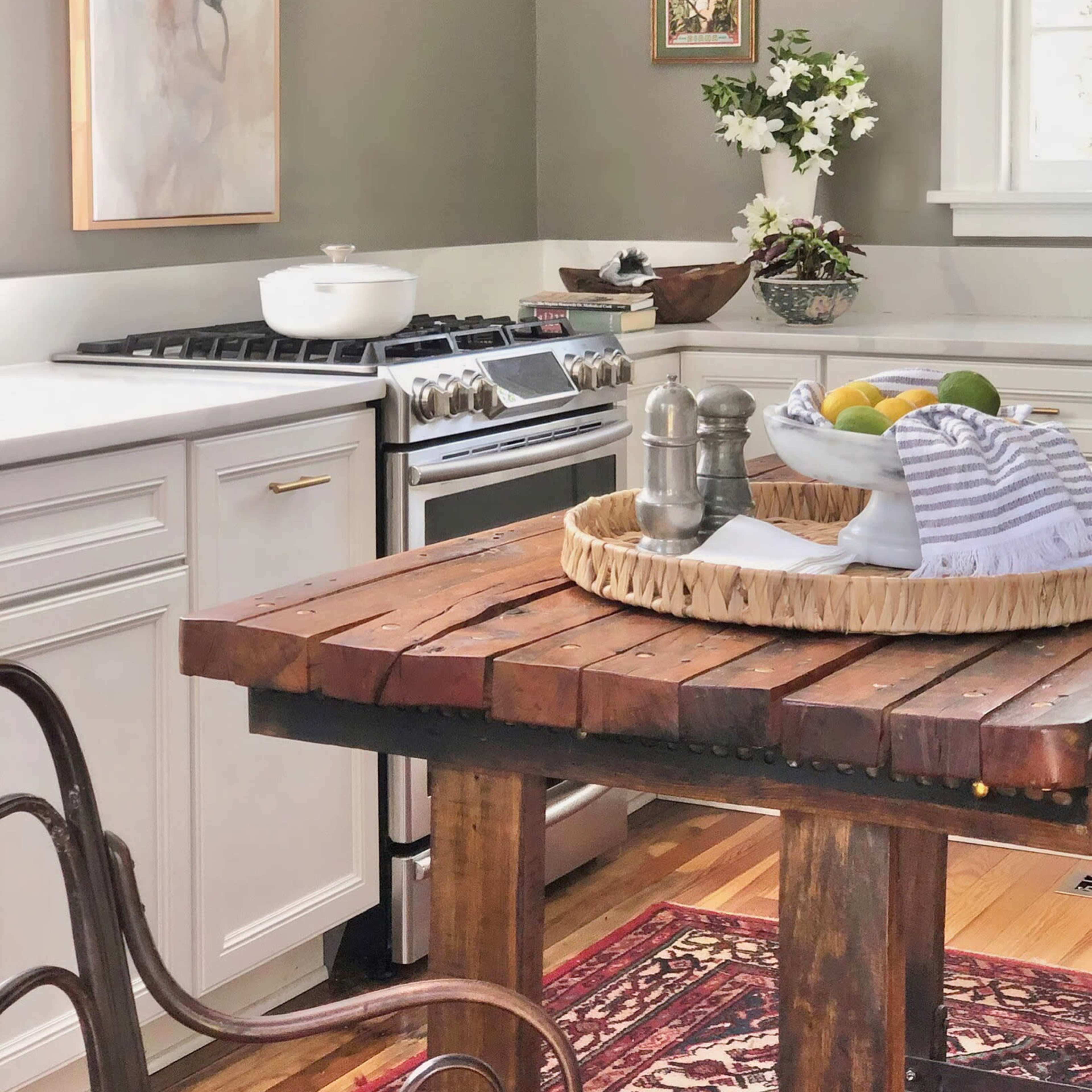 A modern kitchen with a wooden dining table, gas stove, and various kitchen decor, including fruit and flowers.