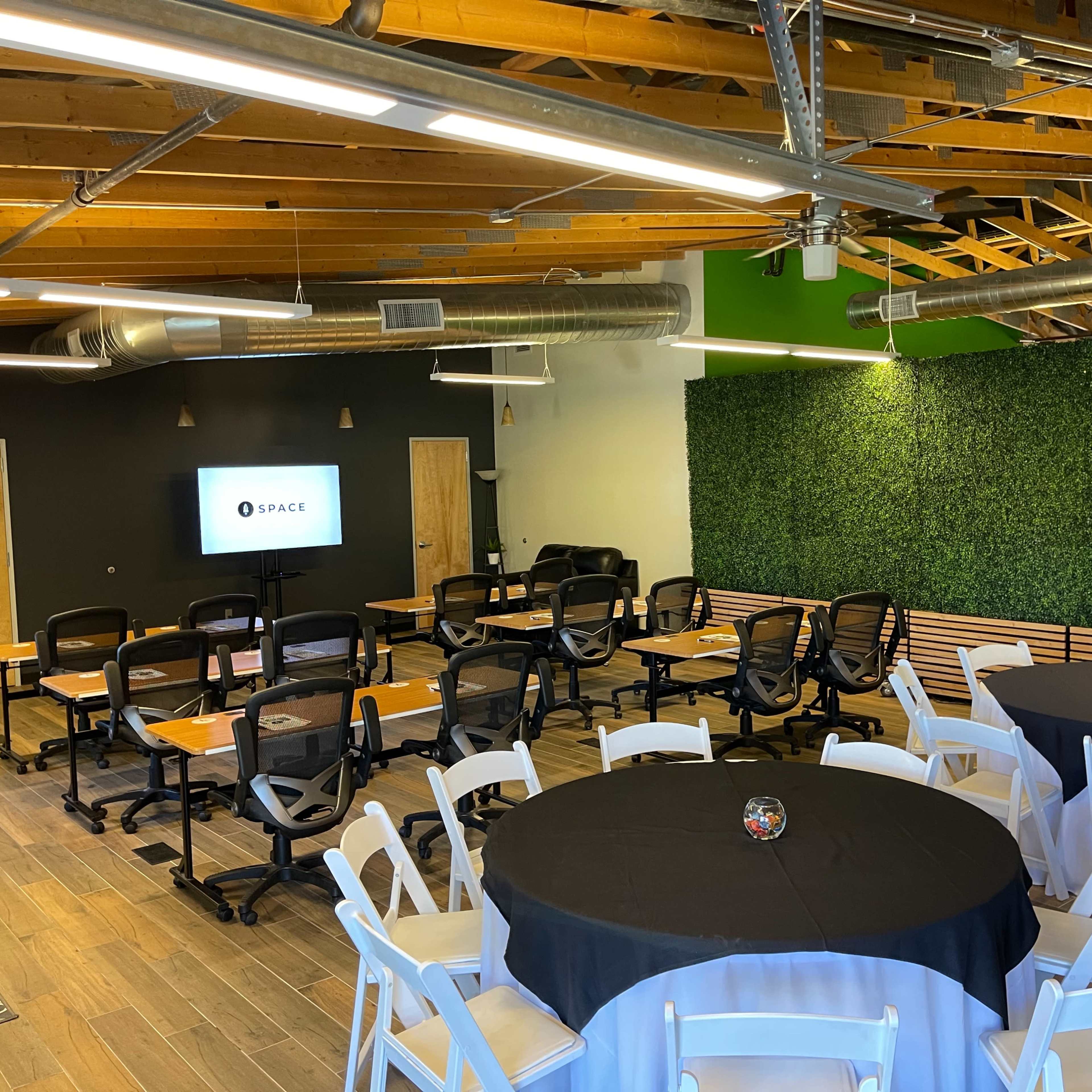 A modern meeting room with rows of black chairs and tables set up, alongside a green wall and a screen displaying the word "SPACE."