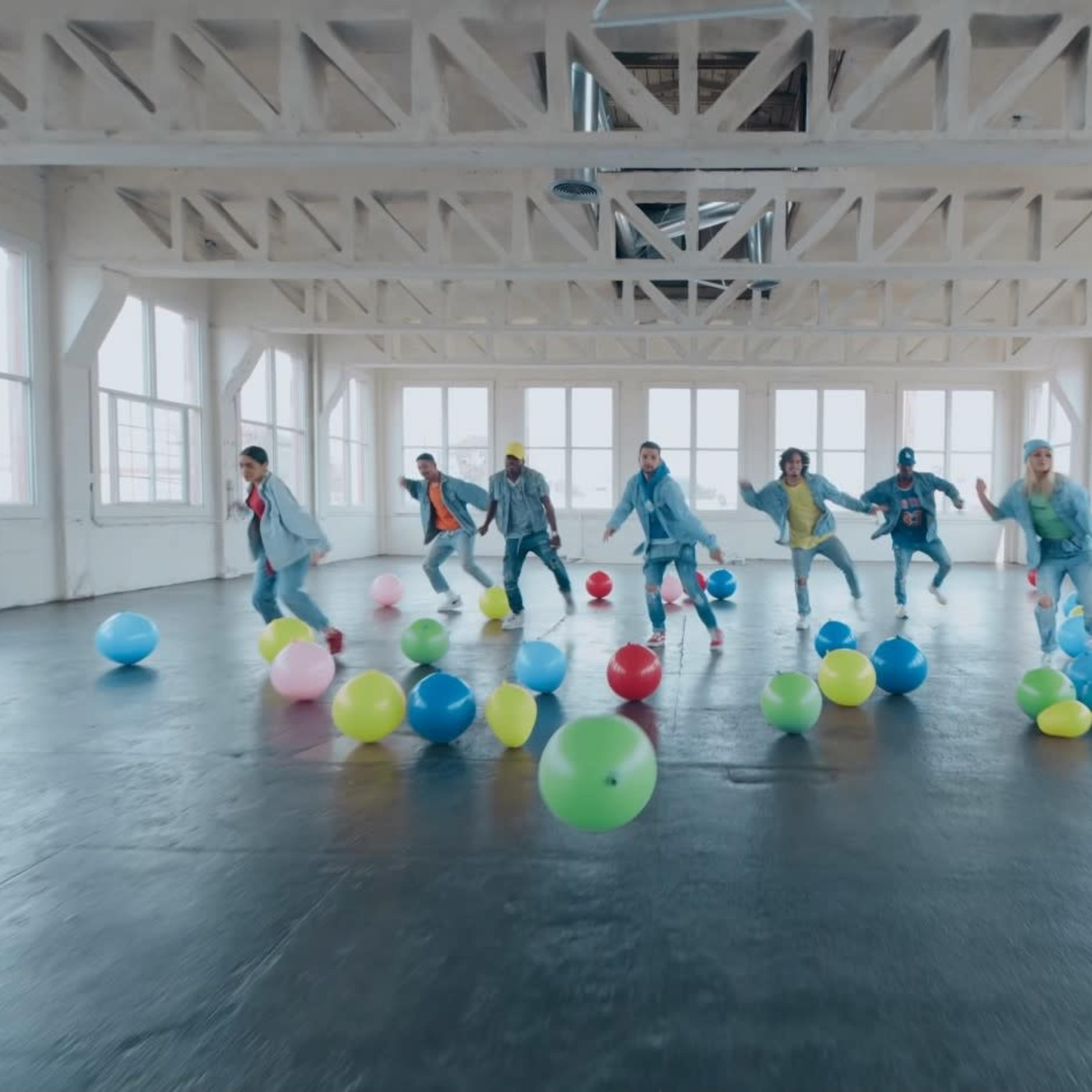 A group of dancers performs in a spacious, well-lit room filled with colorful balloons.