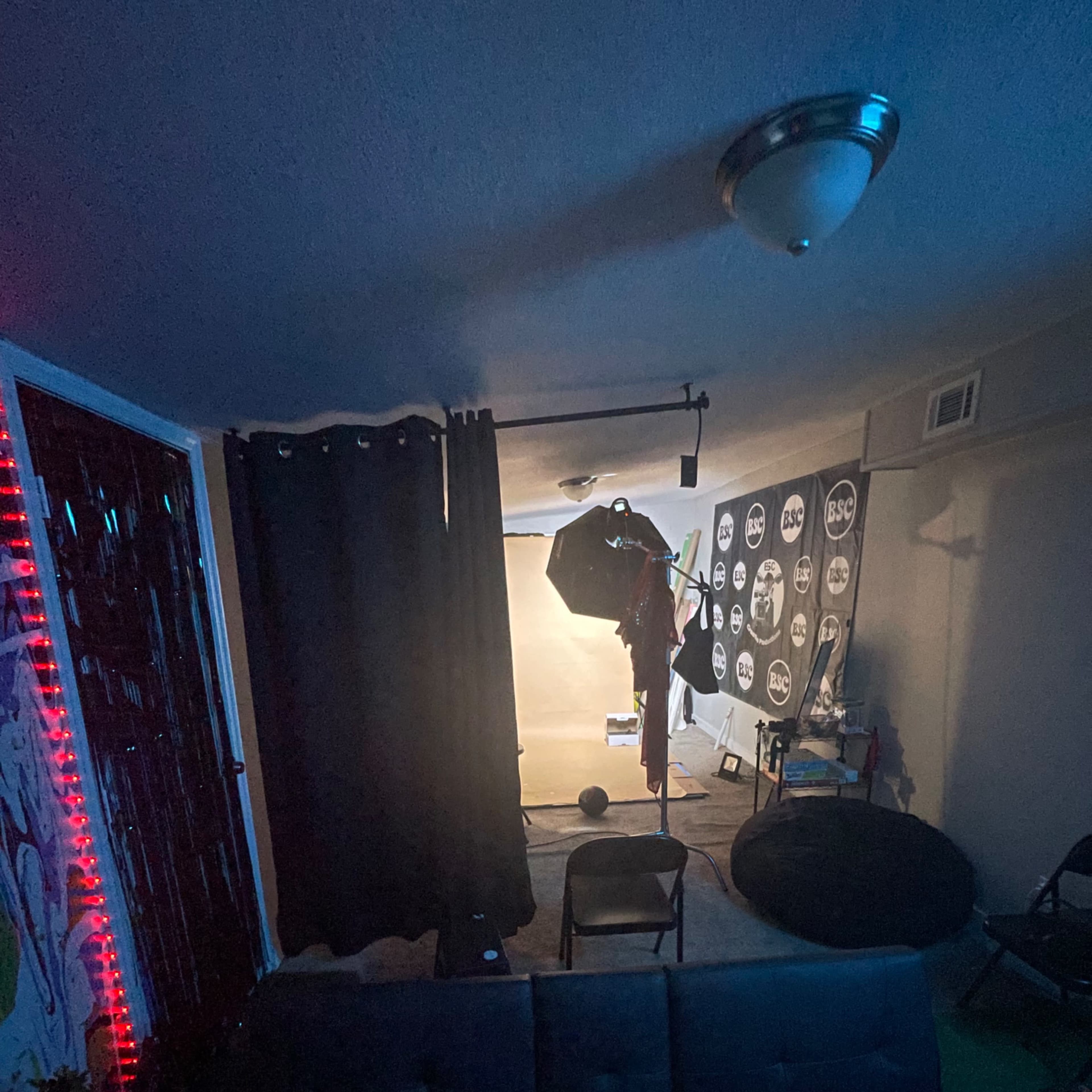 A dimly lit room features a photography setup with a backdrop, lighting equipment, and a few scattered chairs.
