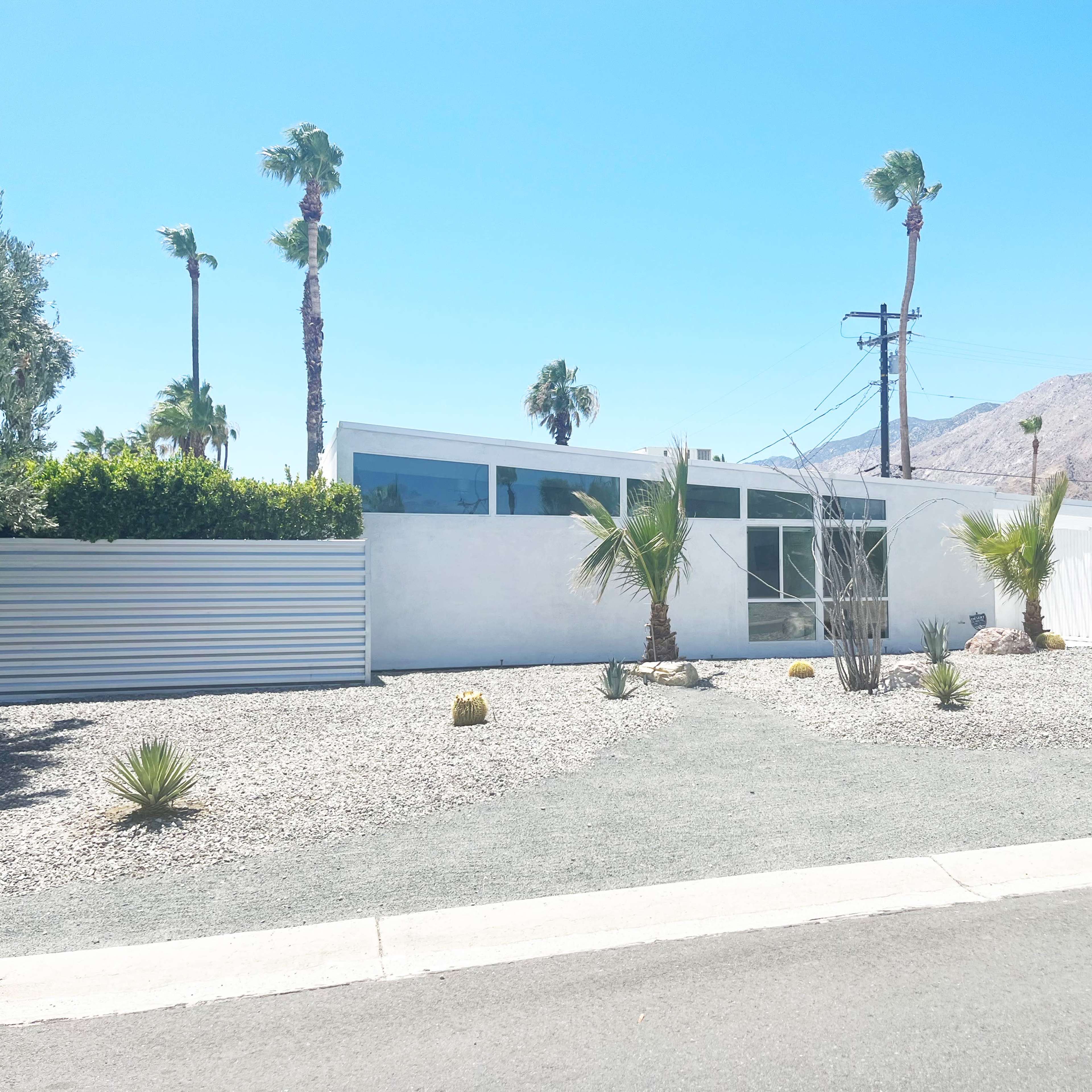 A modern, one-story house surrounded by palm trees and gravel landscaping in a desert setting.