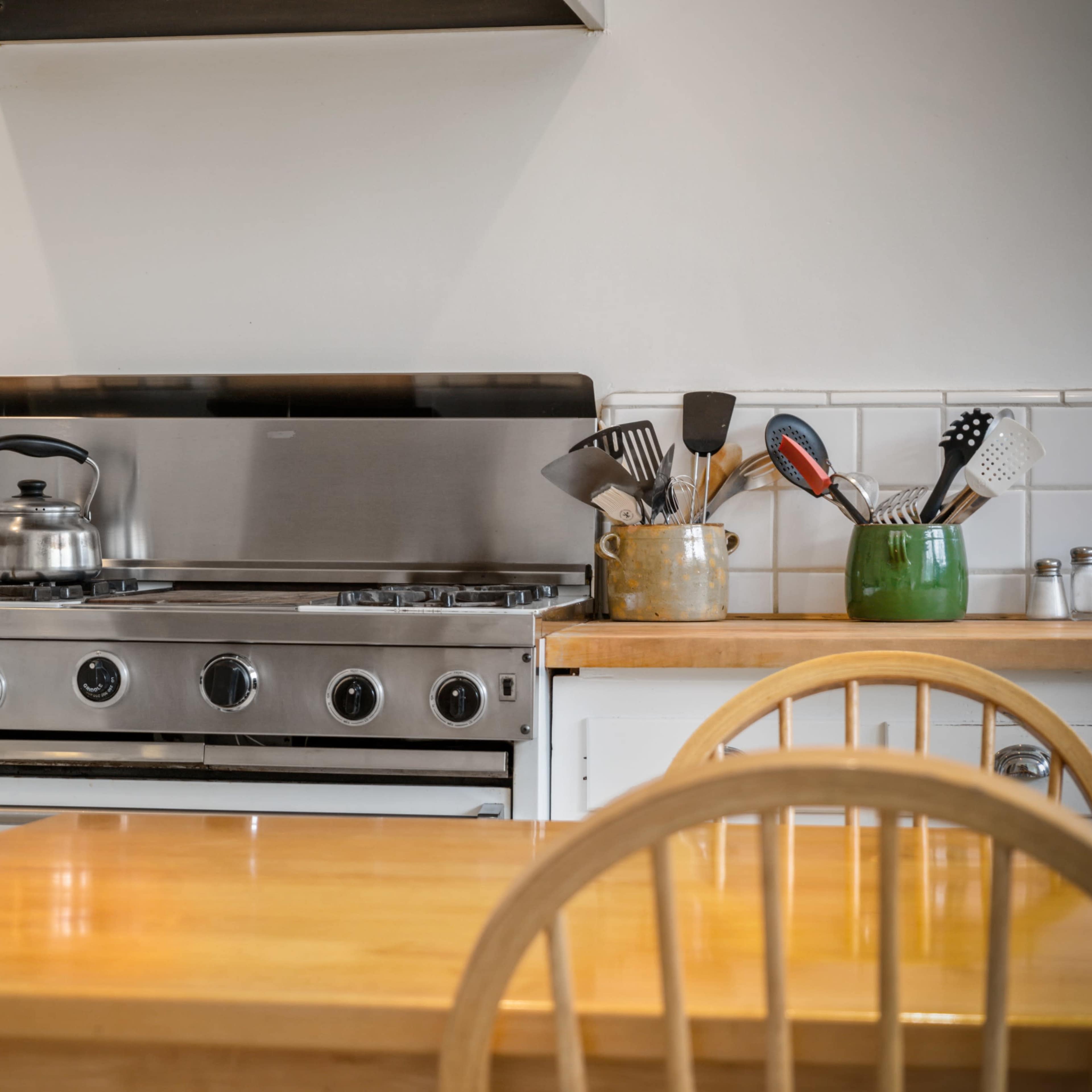 A stainless steel stove and countertop are positioned in a kitchen with a wooden dining table and chairs nearby.