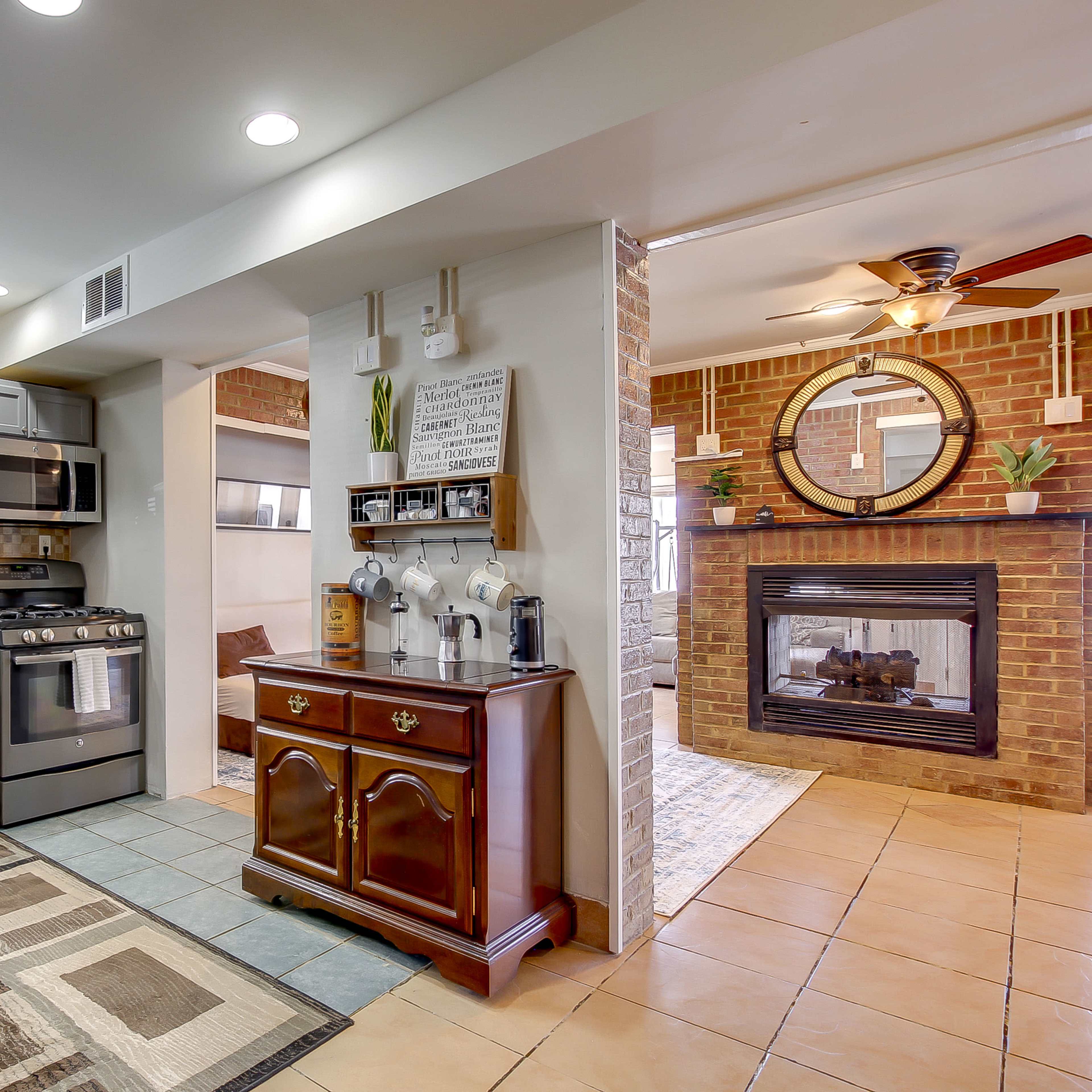 A modern kitchen with stainless steel appliances and a cozy living area featuring a brick fireplace and a round mirror.