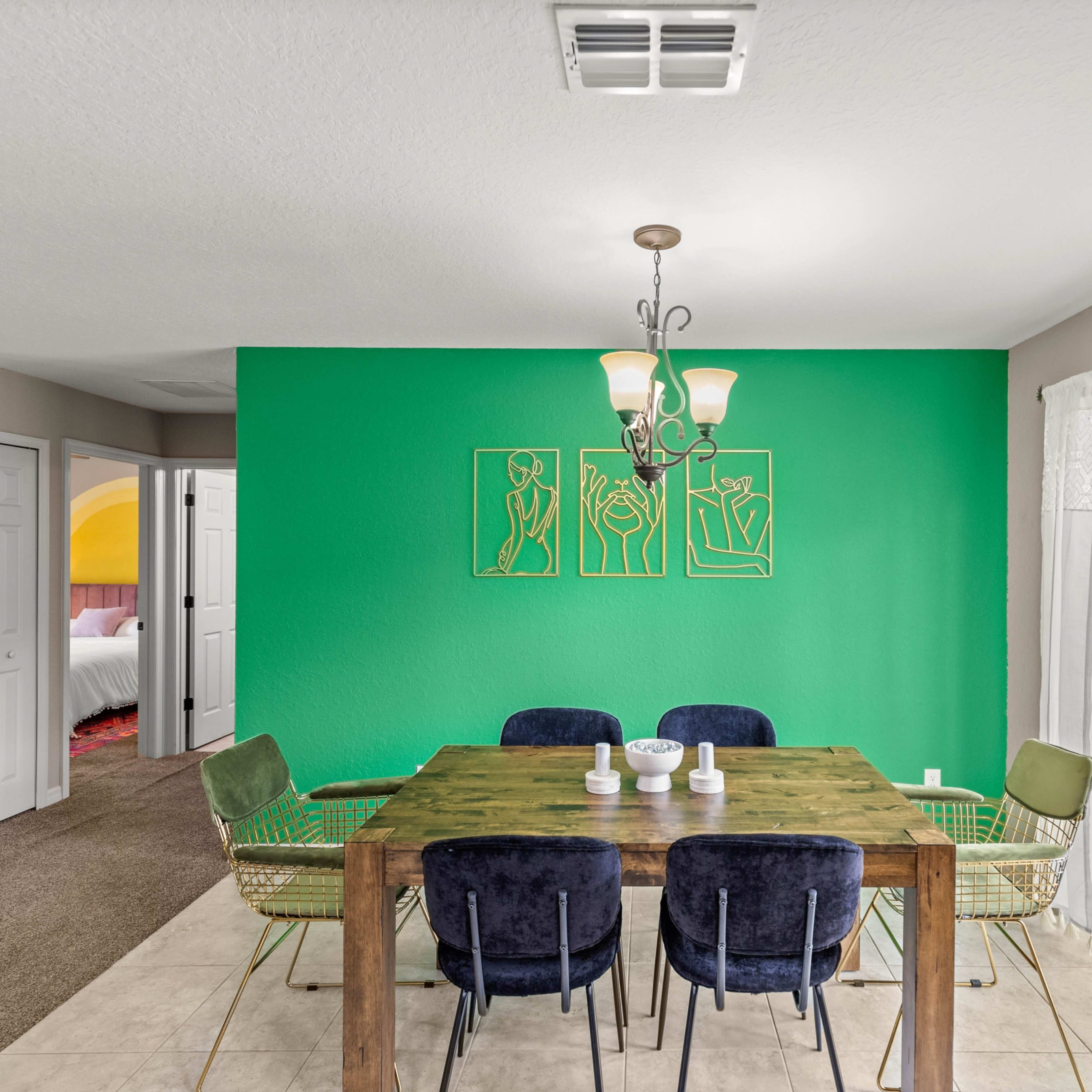 A dining area features a green accent wall, a wooden table surrounded by chairs, and a sliding glass door leading to an outdoor space.