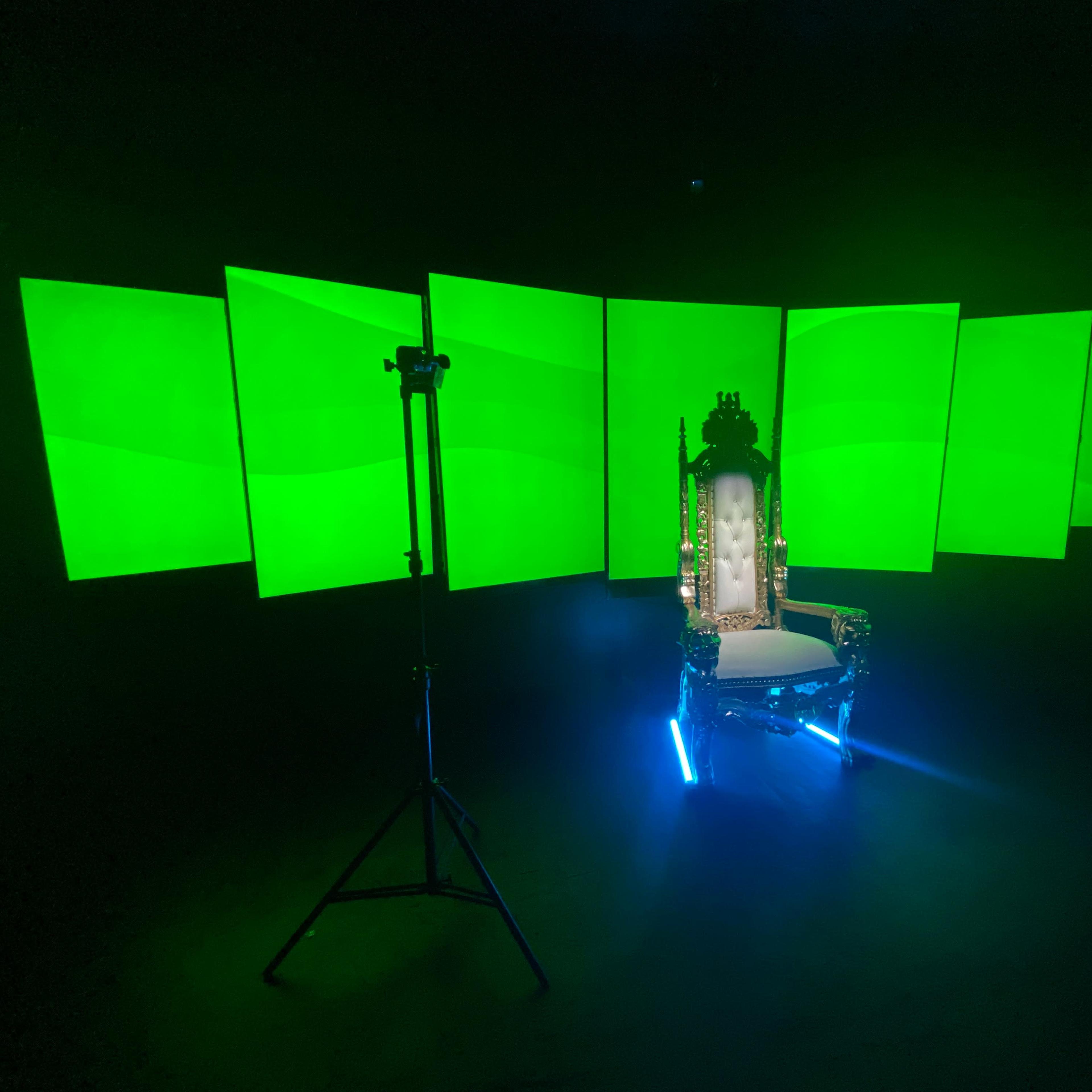 A throne illuminated by blue lights, surrounded by large, green backlit panels in a dark setting.