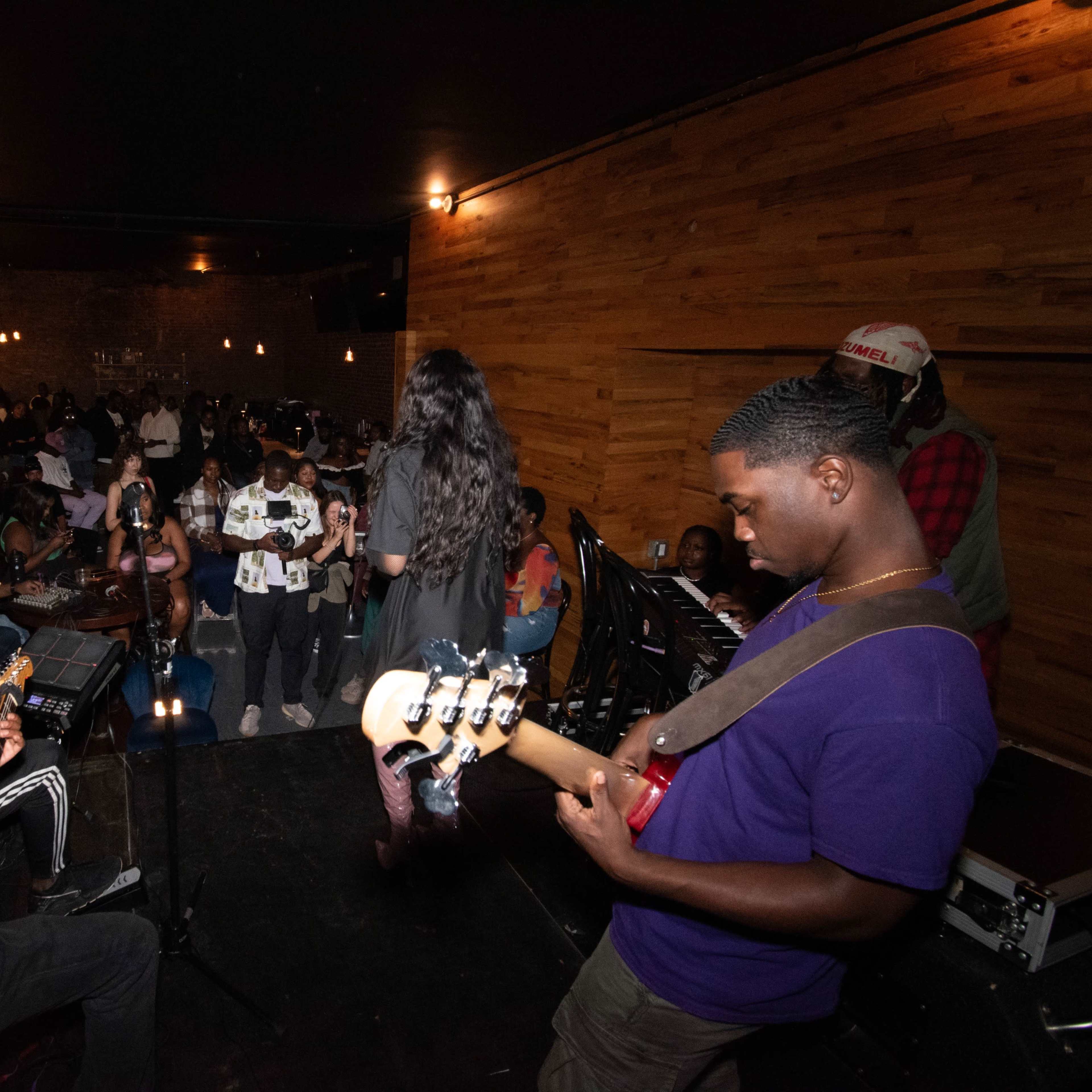 A live band performs on stage while an audience listens and engages in a dimly lit venue.
