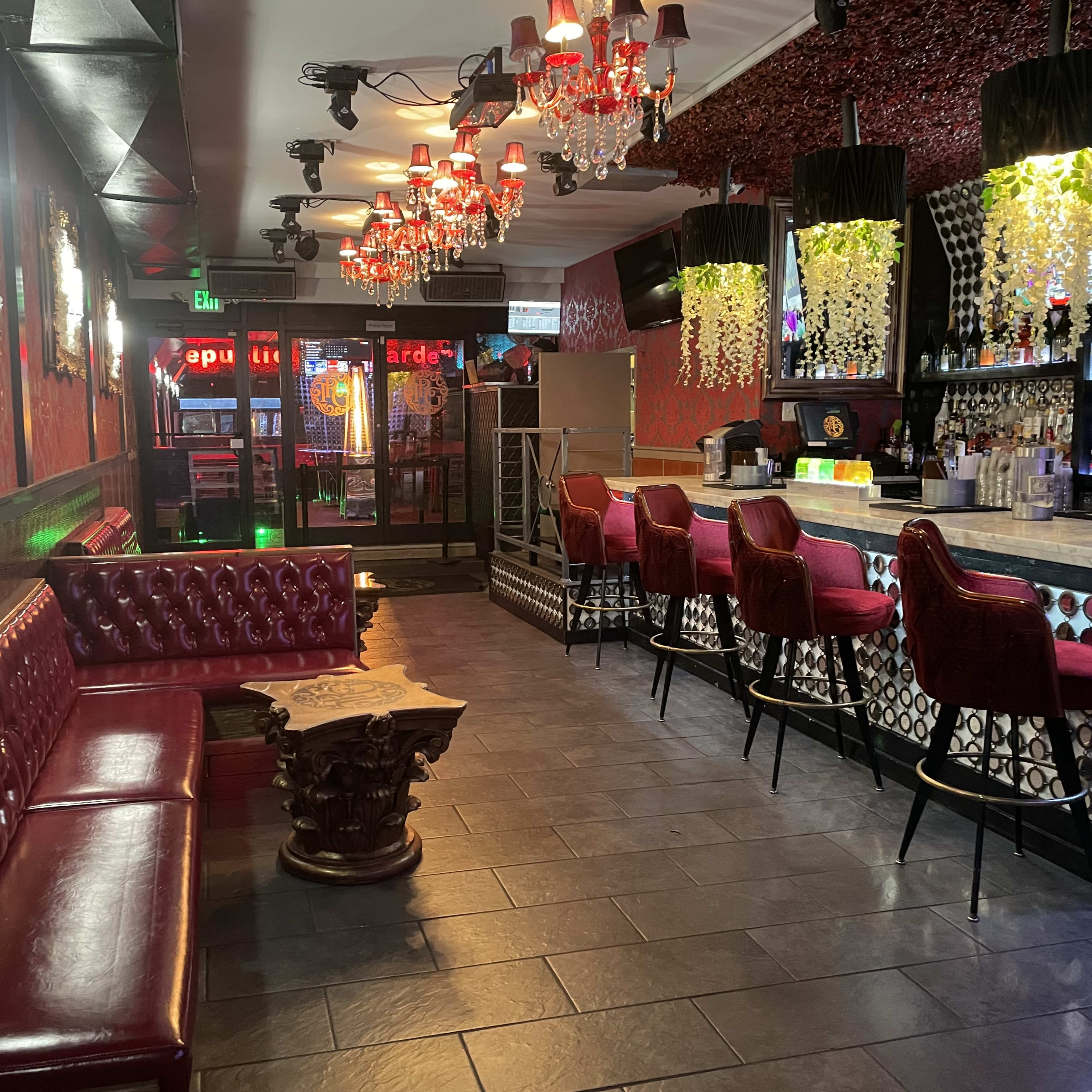The interior of a bar with red leather seating, a dark tiled floor, and illuminated chandeliers hanging overhead.