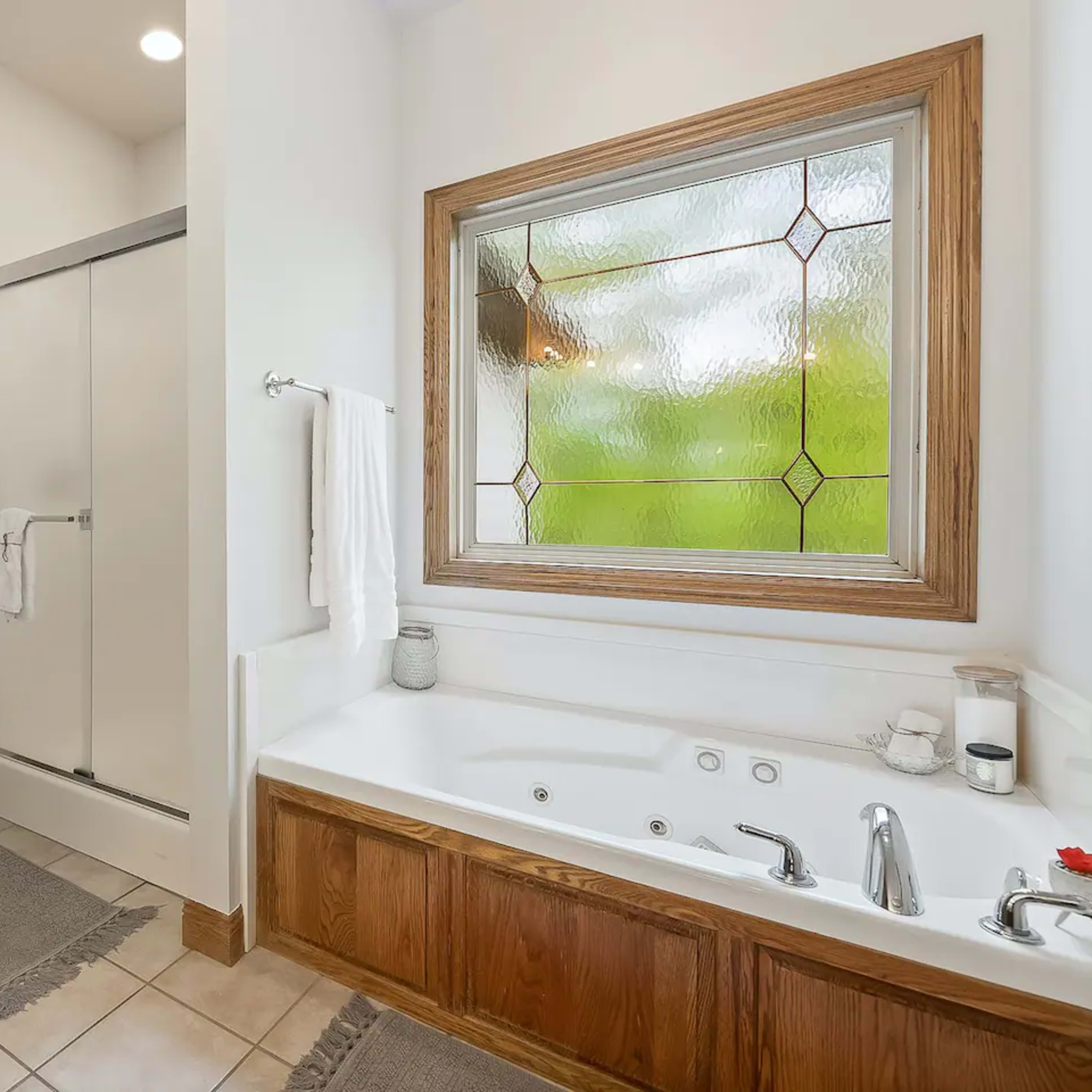 A bathroom with a glass shower, a jetted tub, and a decorative window.