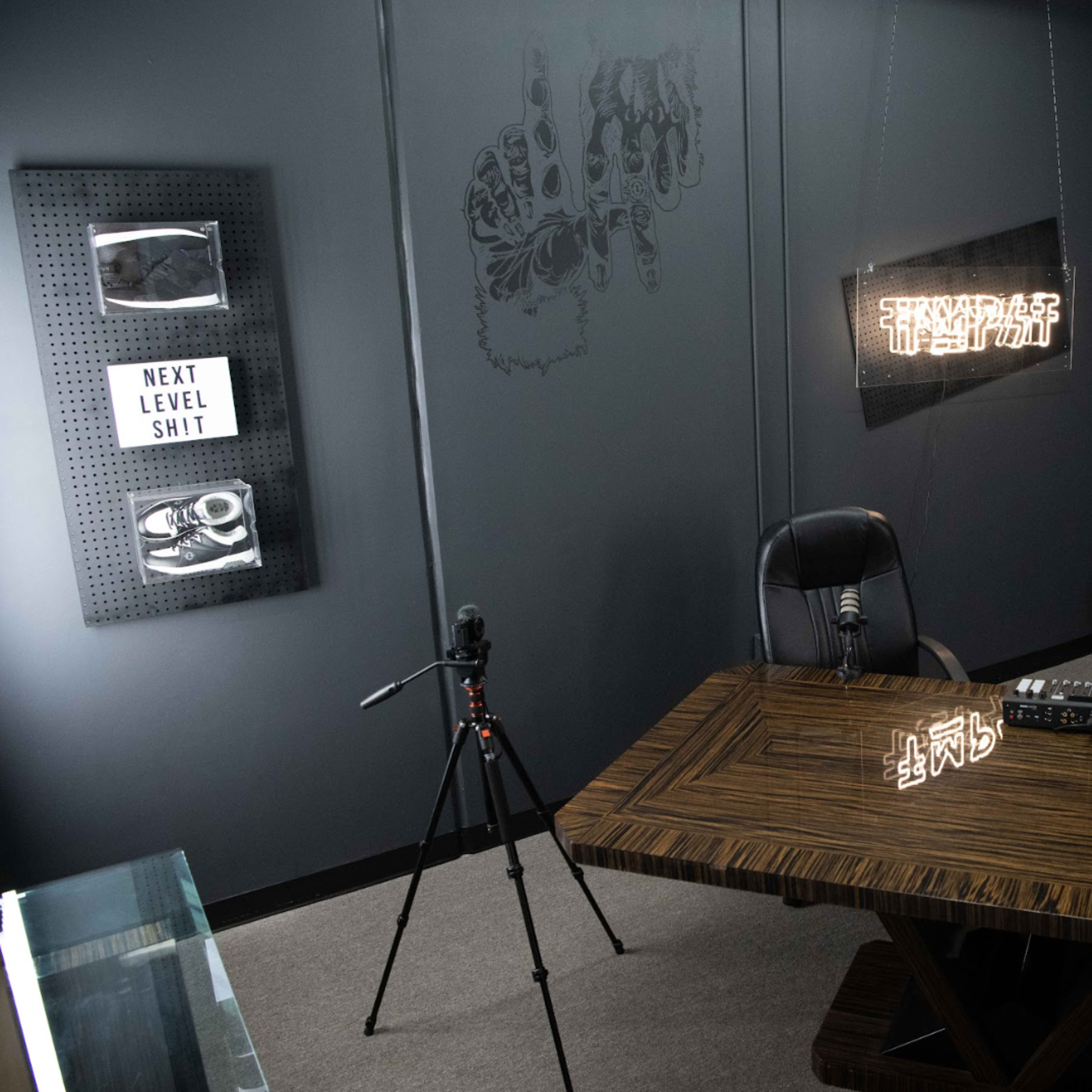 A recording studio setup with a wooden table, two chairs, microphones on stands, and decorative wall art.