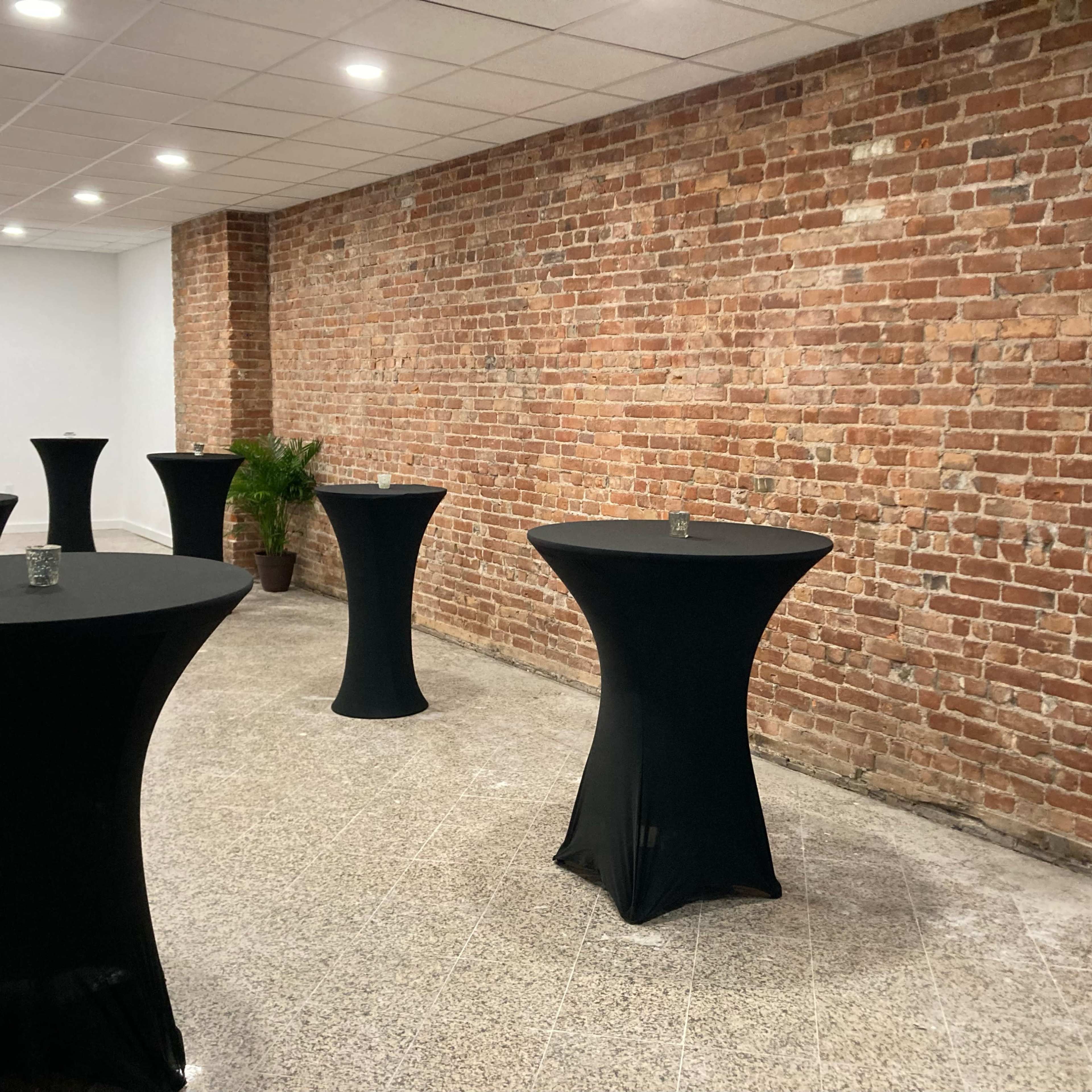 A spacious room with several tall black cocktail tables set against a brick wall.